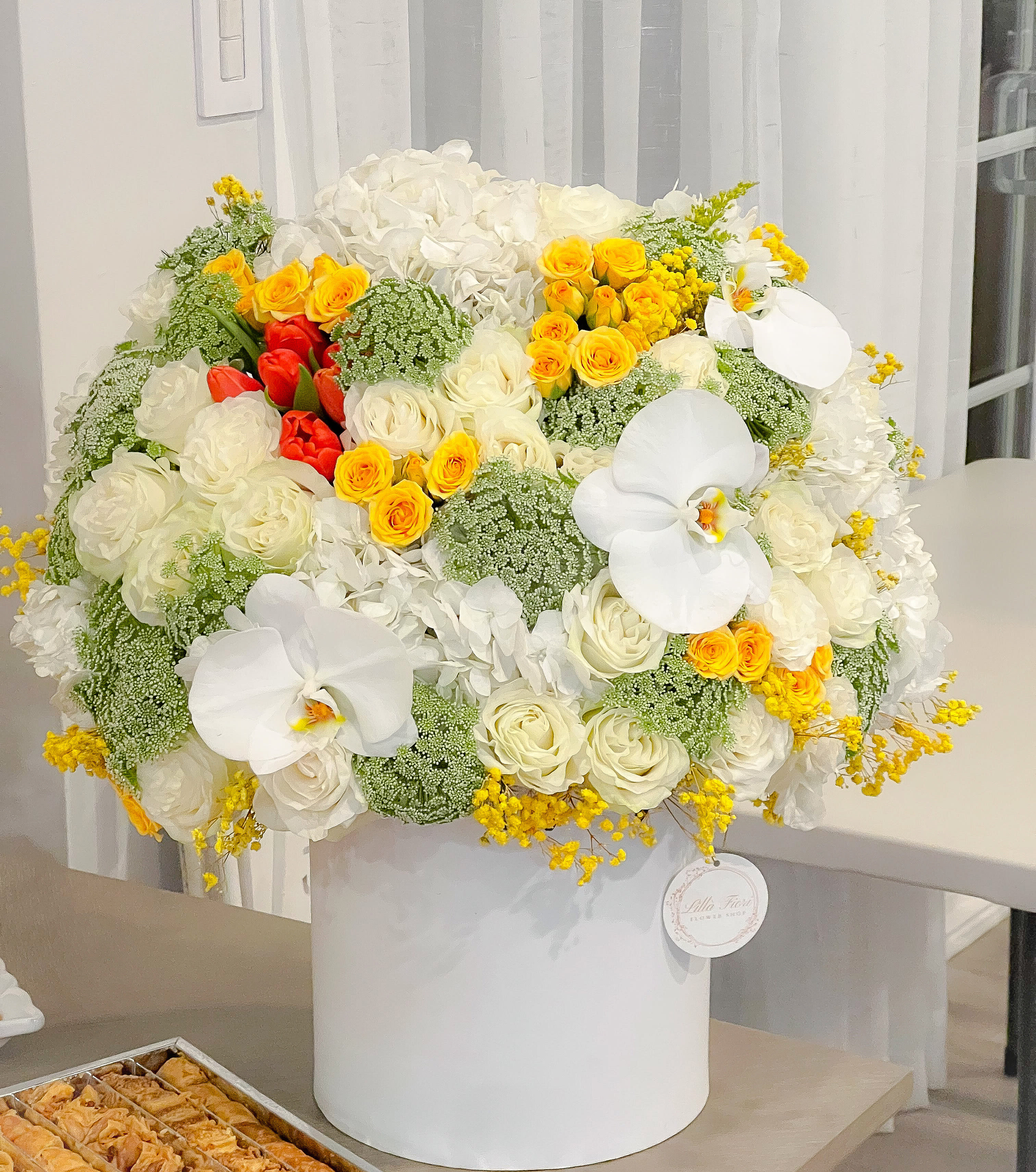Large white floral arrangement with yellow and red roses in a white hatbox