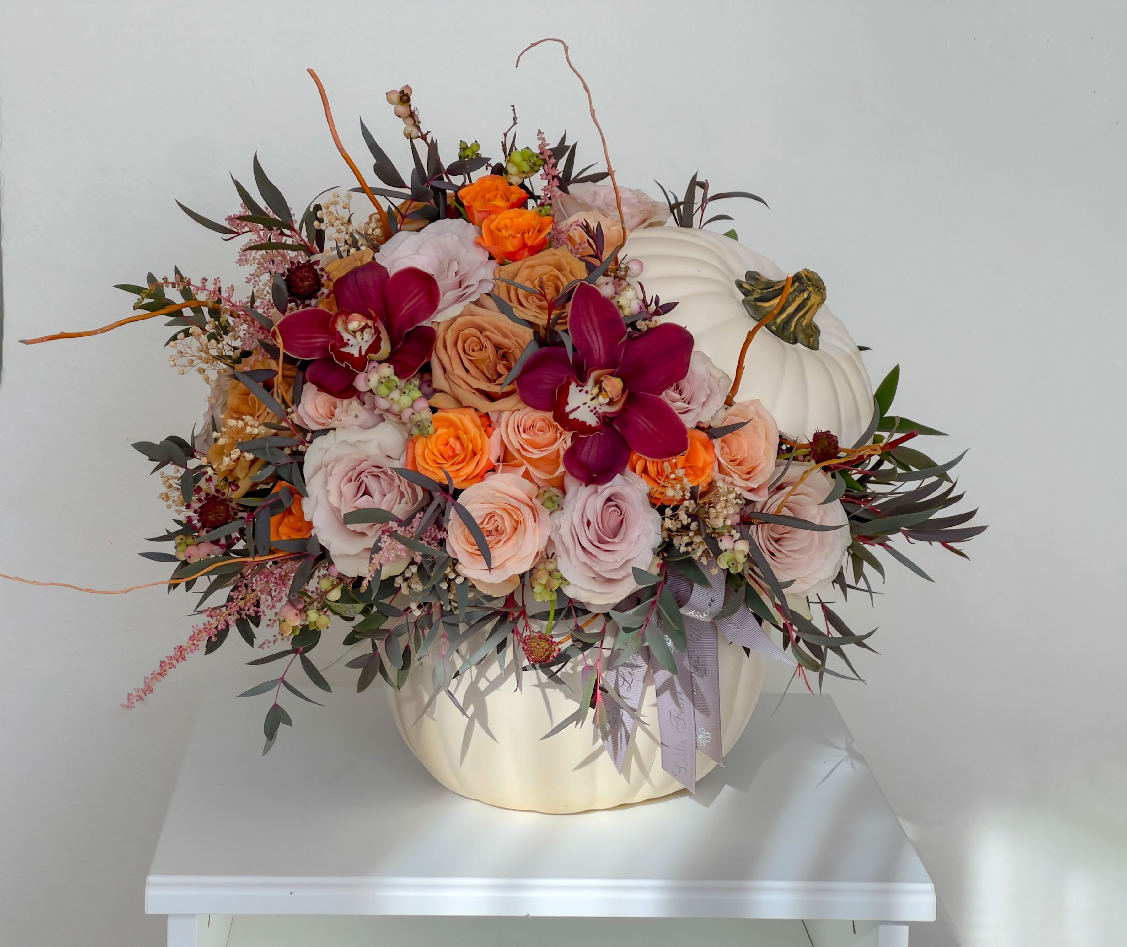 Floral arrangement in a white pumpkin container with roses and orchids