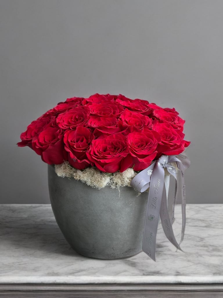 Red roses arranged in a gray pot with a ribbon bow