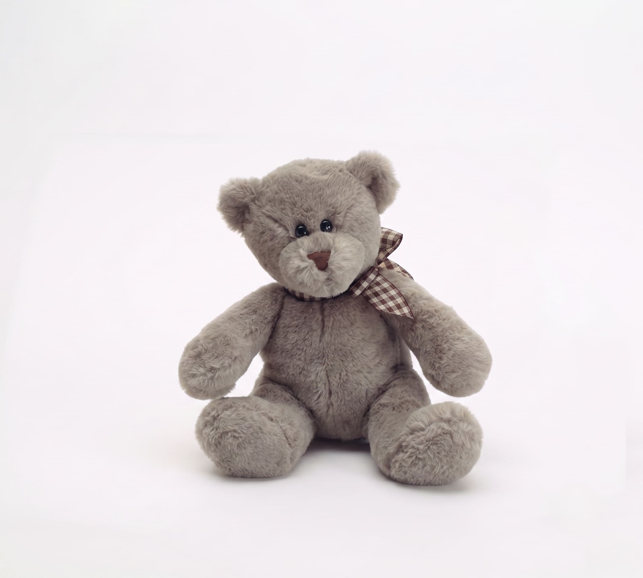 Gray teddy bear with a checkered ribbon sitting on a white background