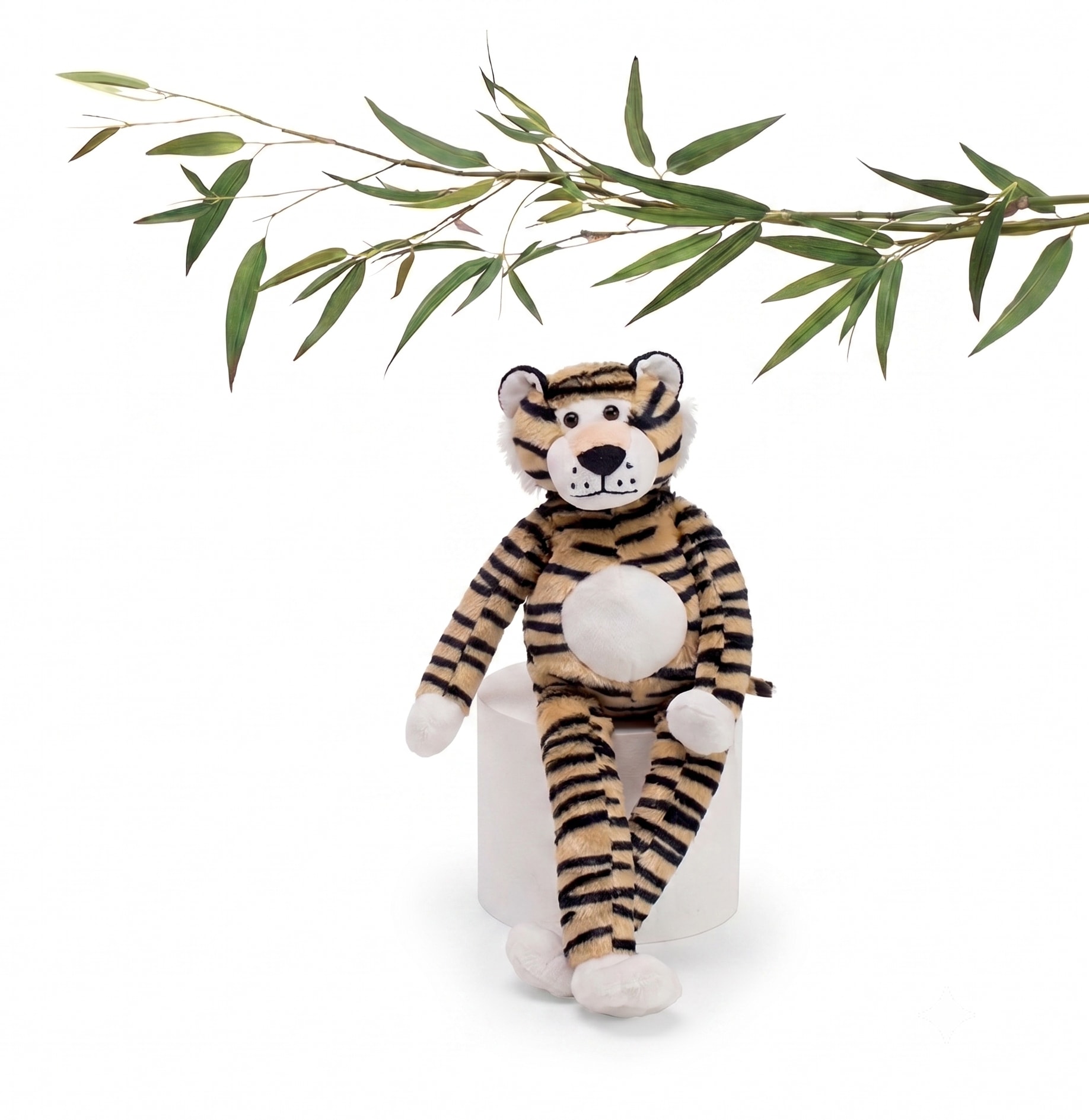 Plush tiger sitting on a white cylinder with a bamboo branch above