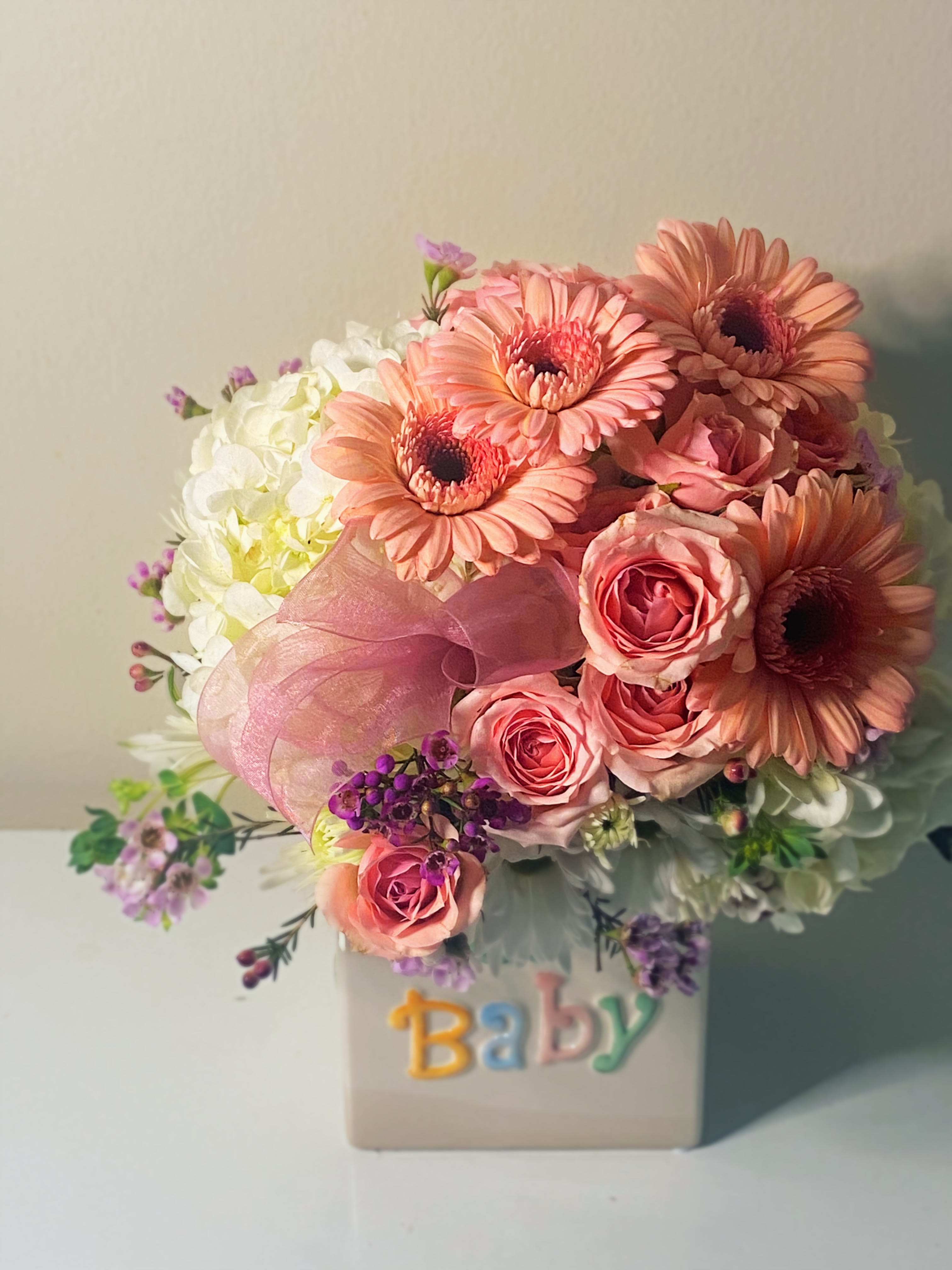 Baby girl - Baby girl is a sweet collection of white hydrangea, pink gerber daisies and pink spray roses stylized with a of touch of pink wax flower adorned with a dainty pink bow. 5 in ceramic container approximate size of arrangement is  9 to 10 in wide and 11 to 12 inches high. Perfect sized gift to congratulate new parents. 