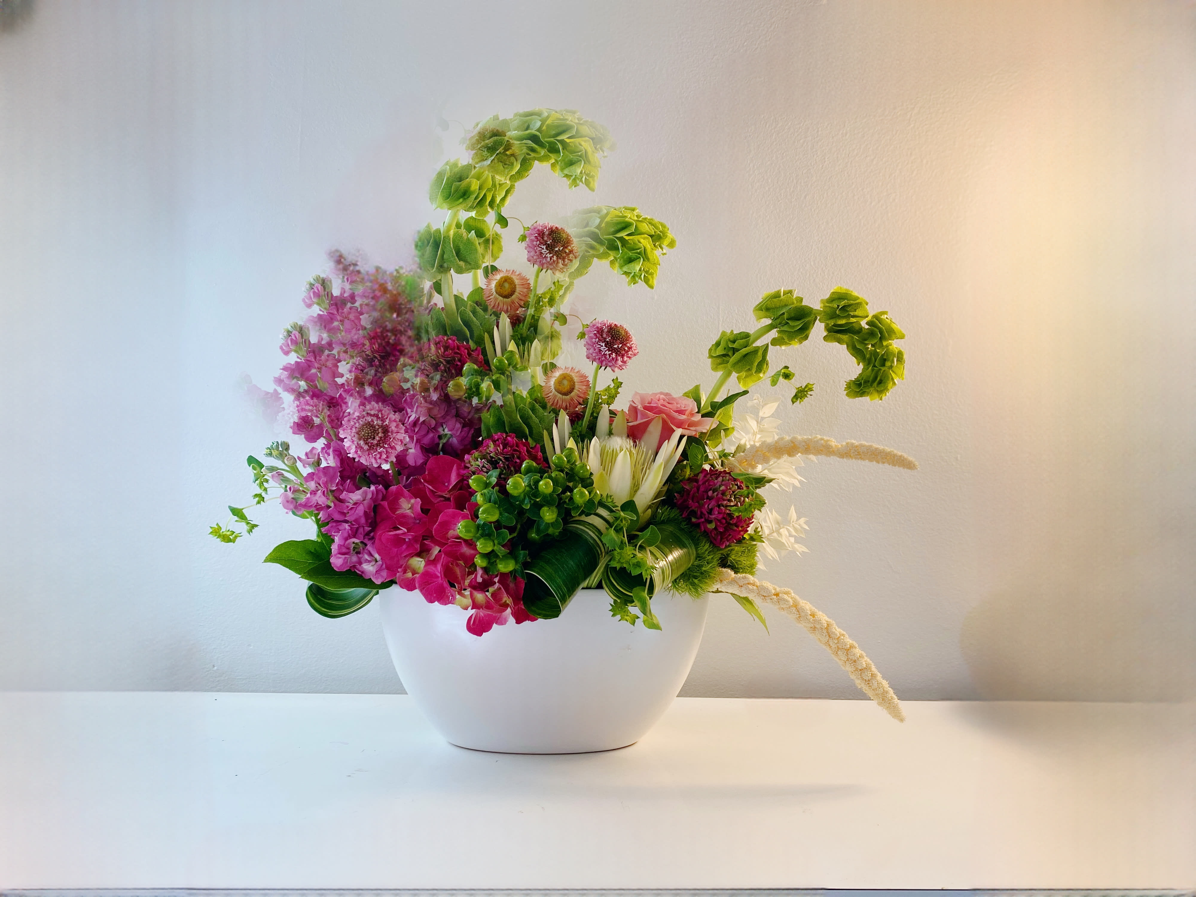 The Bright Hue - Indulge floral arrangement awaiting your style. This modern marvel in a sleek white ceramic boat vase is designed to perfection. You choose 2-3 colors or indulge in all shades of opulent white or radiant yellow. Simply leave special instructions. Elevate your space with sheer elegance today!  We will pick flowers according to color and texture.  