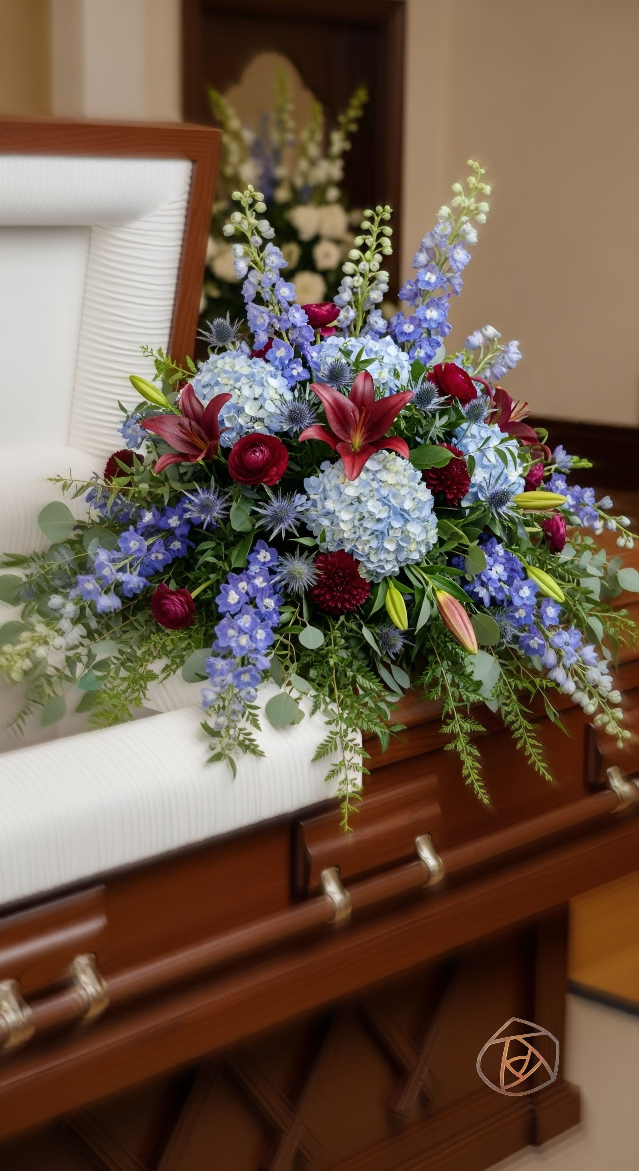 The Admiral Casket Spray - Gorgeous tones of blue to admire, paired with burgandy floral.   Please preorder this item in advance . We use burgundy floral in this design, if ranunculus in burgundy is not available we will replace with similar heart roses