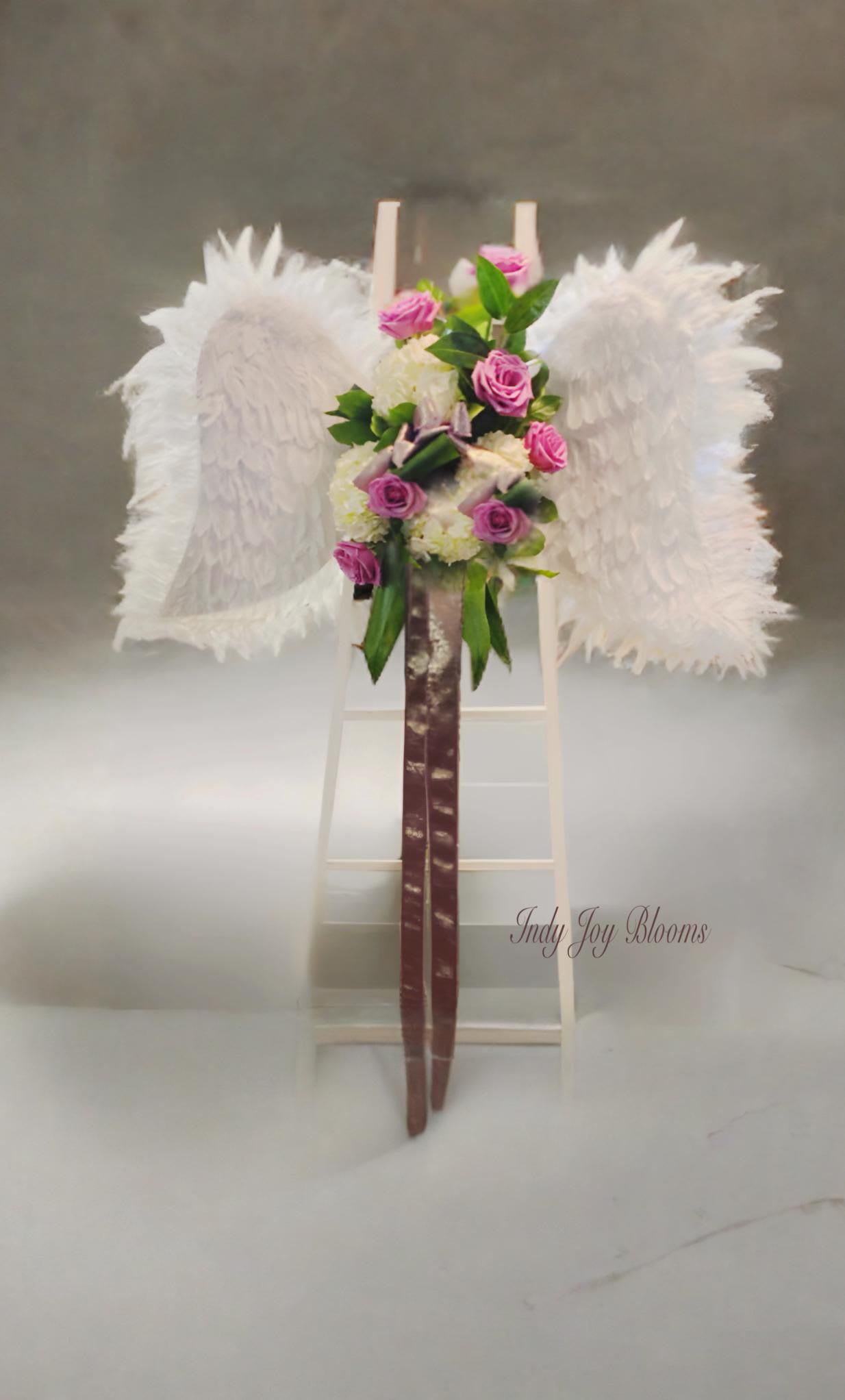 Wings by Indy Joy Blooms - Featherd Angel Wings on a stand with groupings of floral in the colors if your choice. The funeral tribute piece is approximately 4ft x 2.6 ft. Stand is 44 to 60 inches depending on upgrades.  ATTN: this item must be ordered no less that than 3-5 days prior to service.  Please add color preferences to special instructions. 