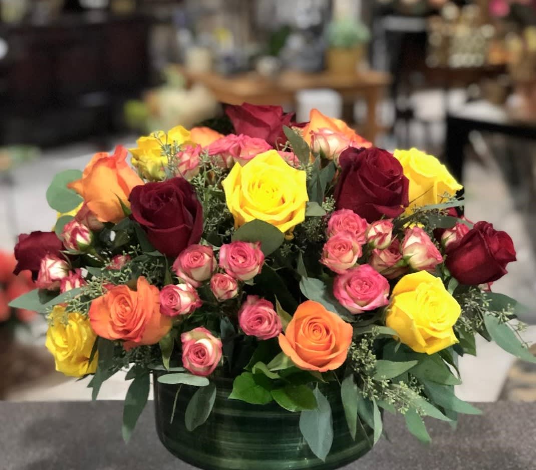 Mixed roses in a low green vase with pink, yellow, orange, and burgundy blooms