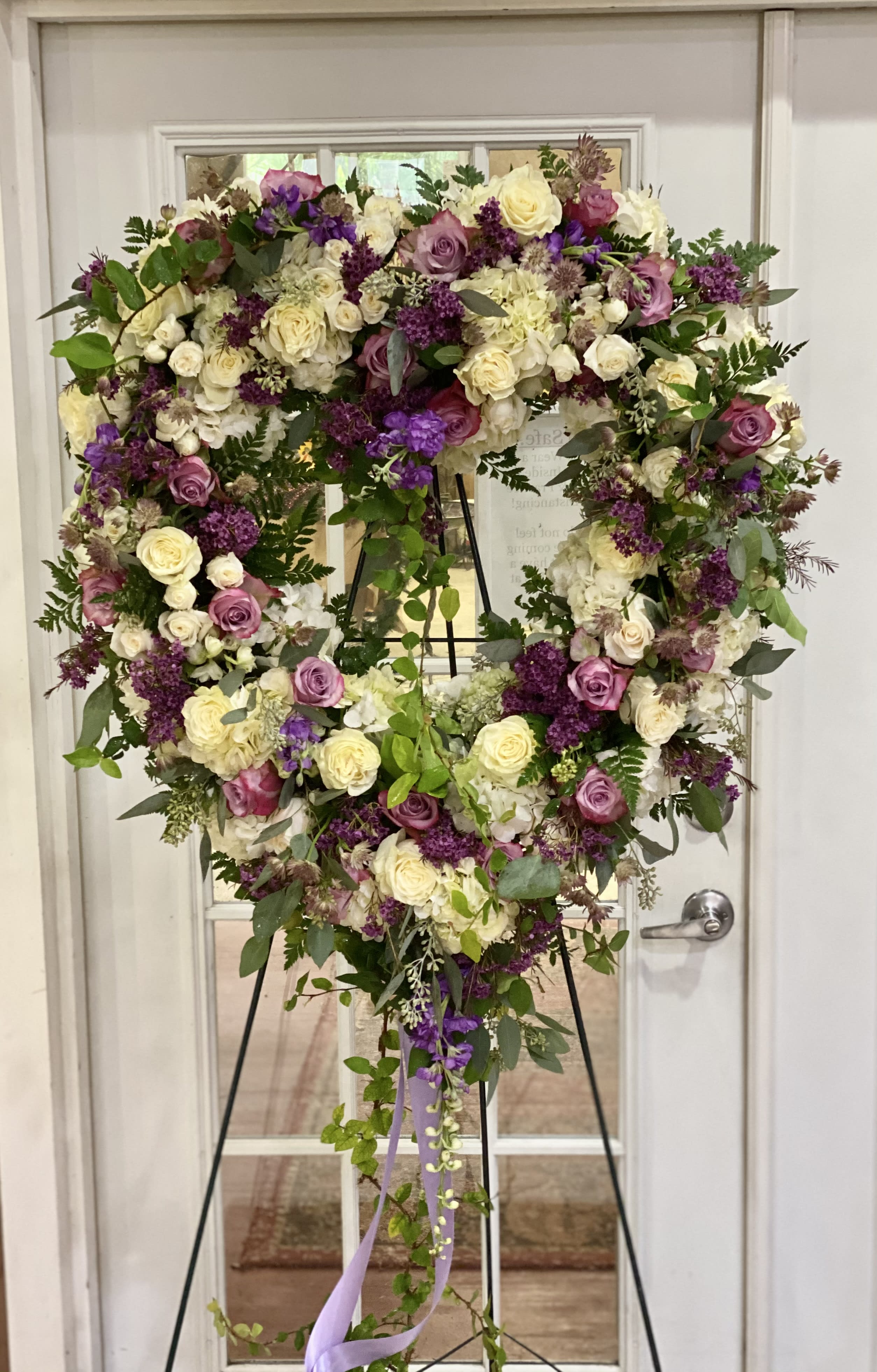 Heart-shaped floral wreath on a stand with cream, pink, and purple roses.
