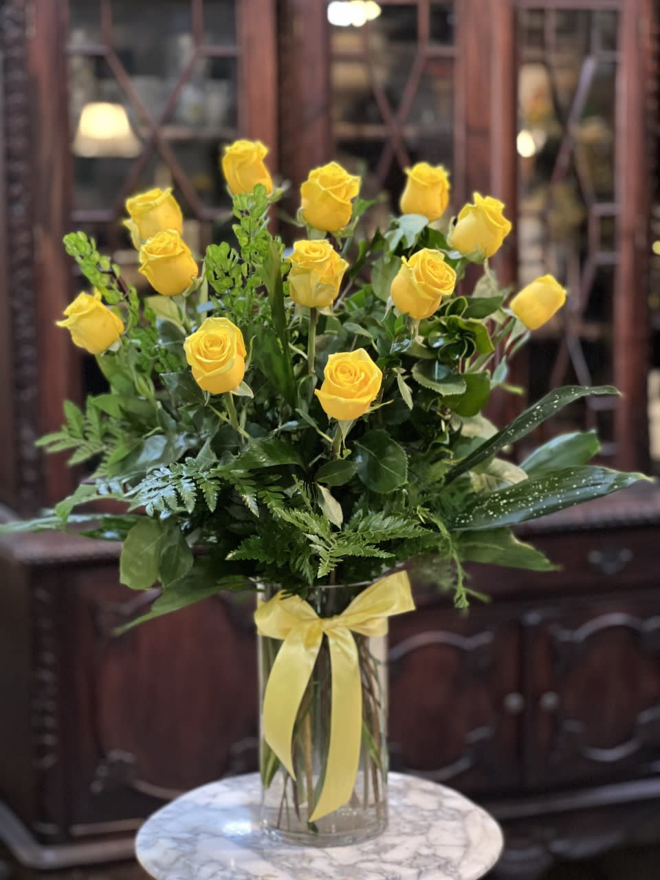 Yellow roses in a clear glass vase with a yellow ribbon