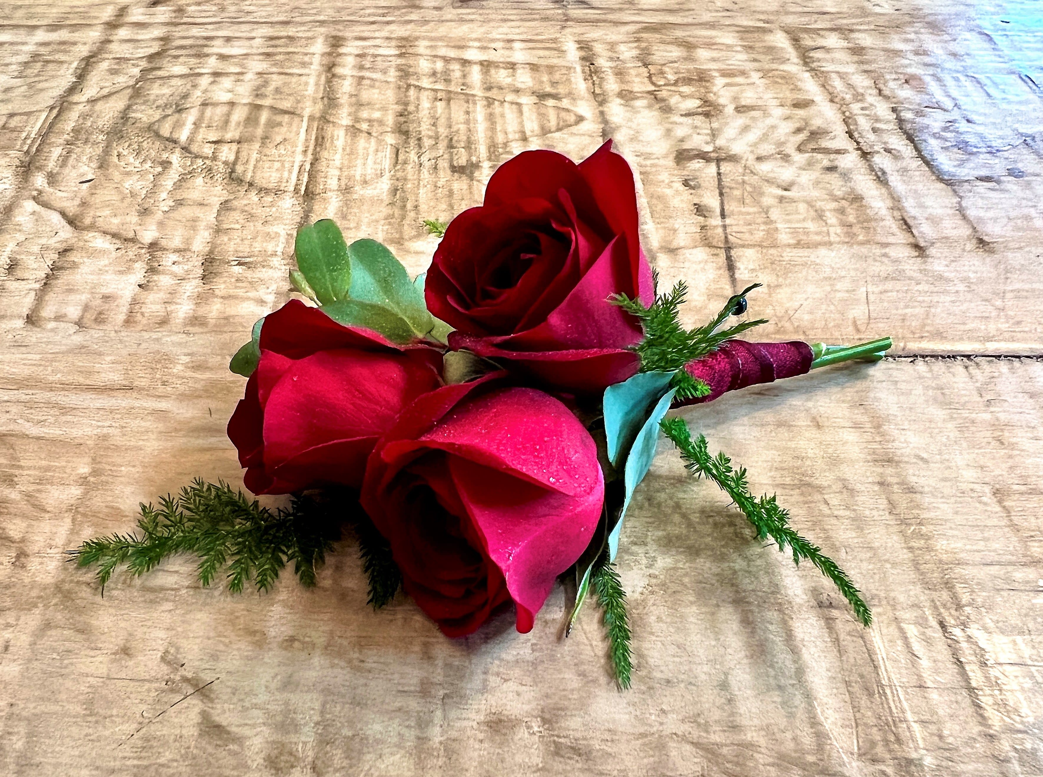 Small bouquet of red roses with greenery on a wooden surface
