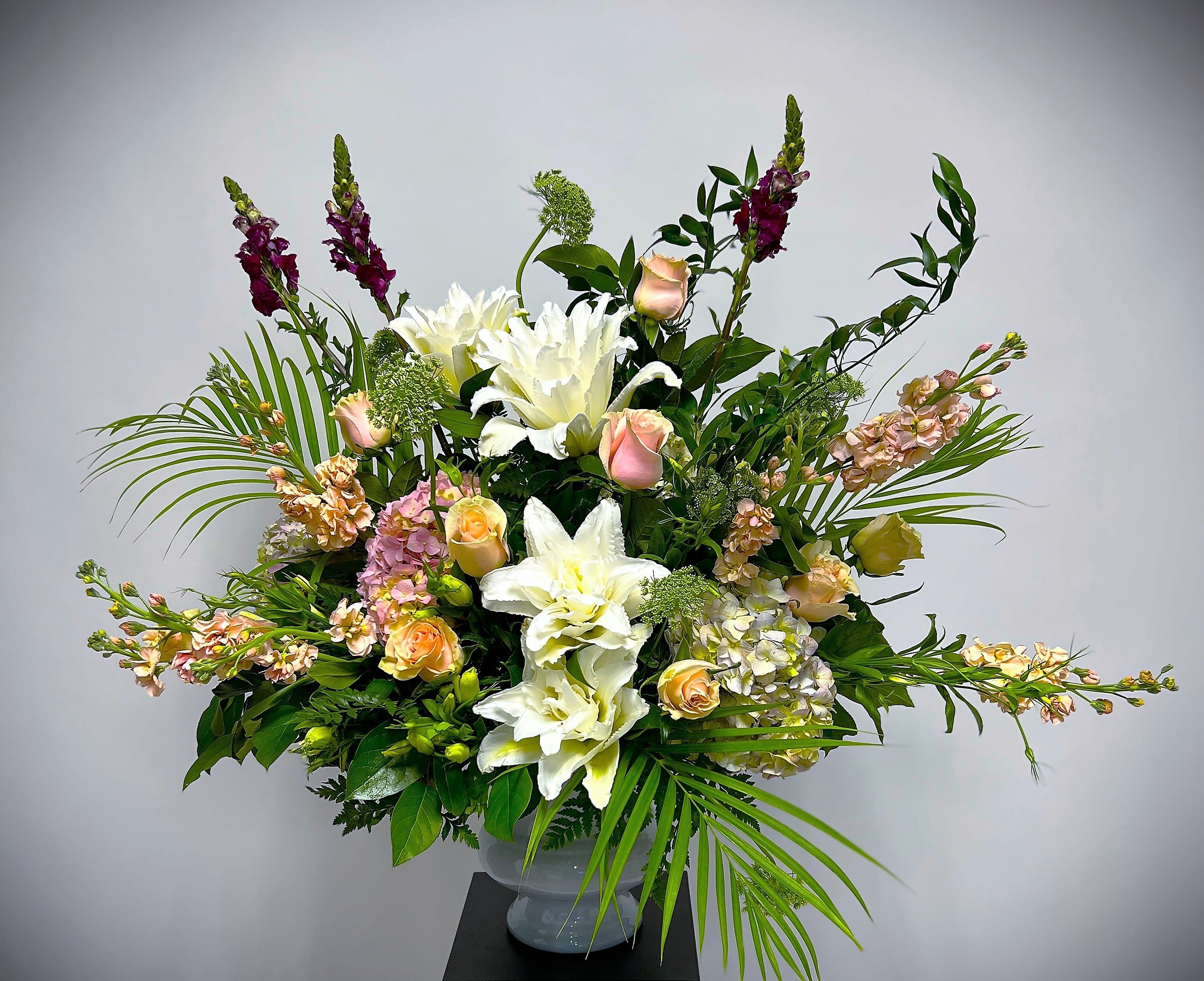 Tall floral arrangement with white lilies, peach roses, and purple spikes in a vase