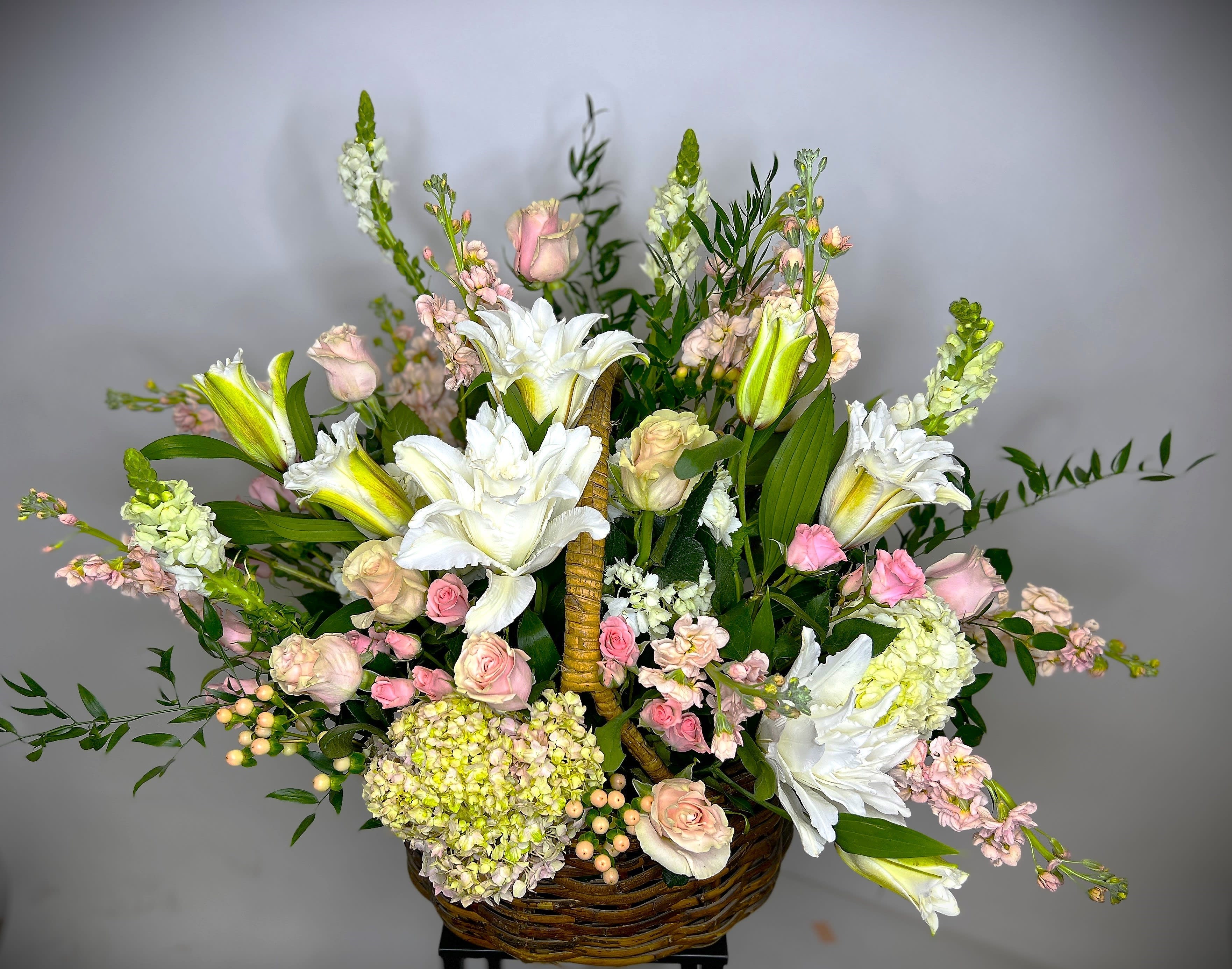 Basket arrangement of white lilies, pink roses, and pale blooms