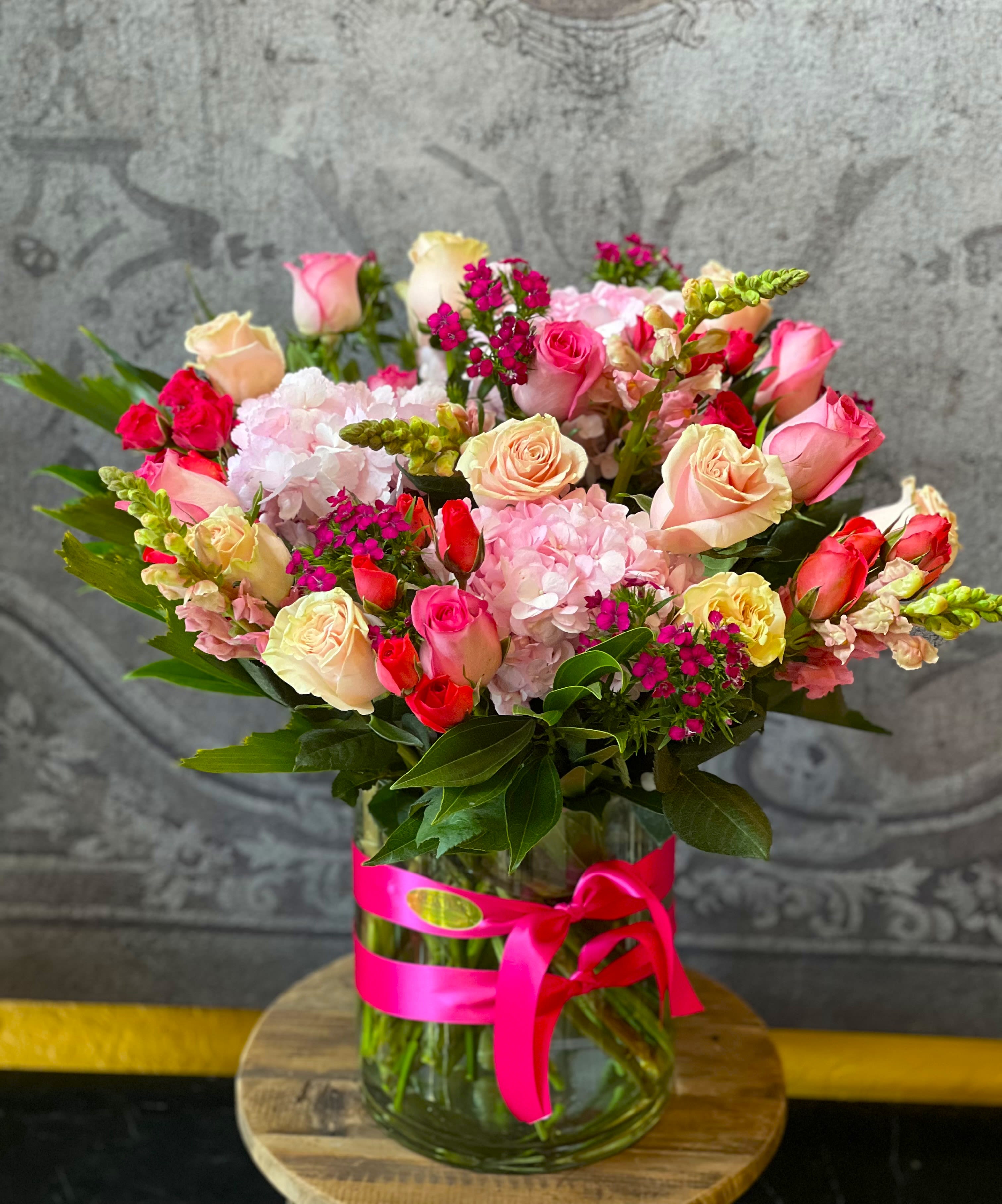 Mixed pink and cream roses in a glass vase with a pink ribbon