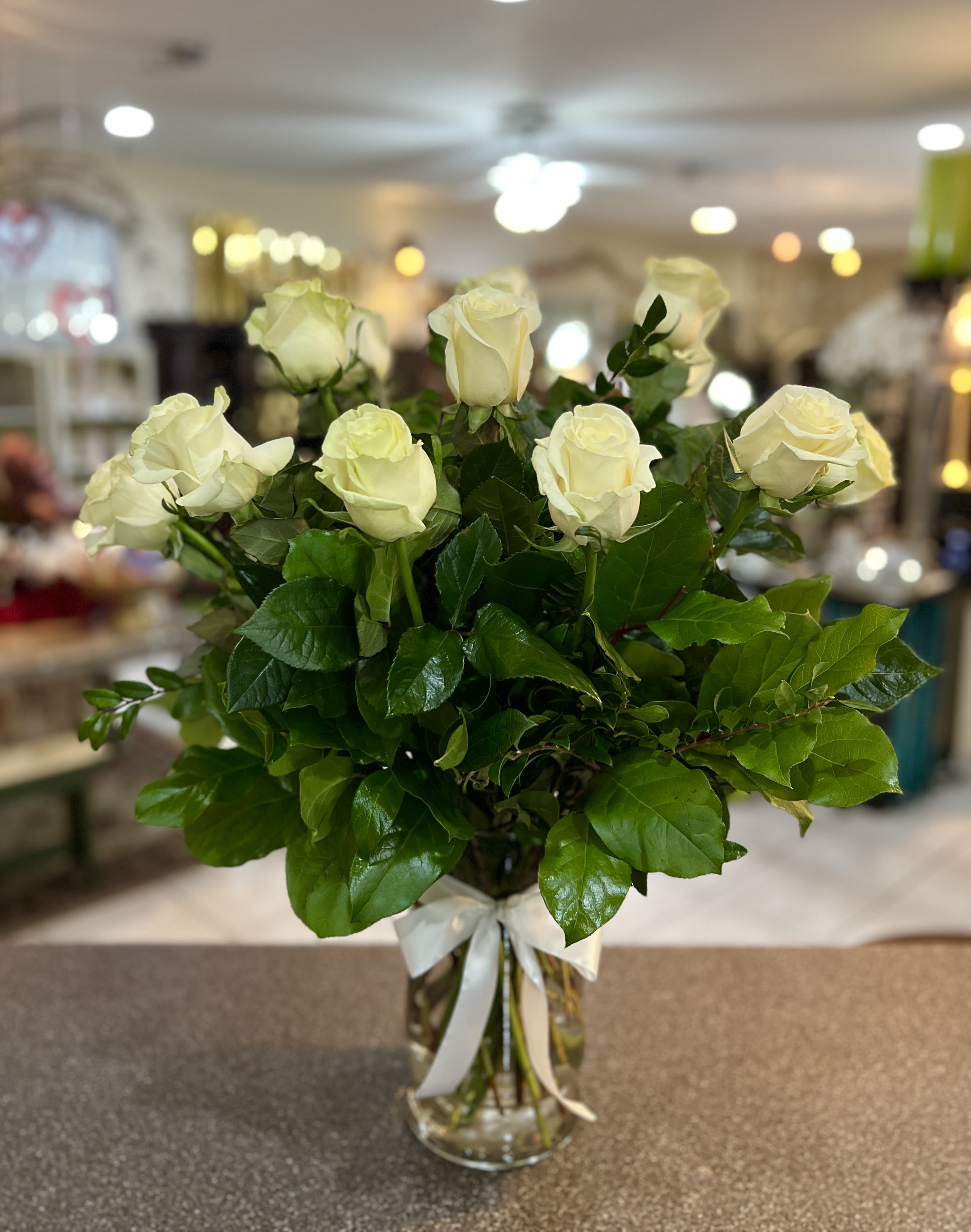 White roses arranged in a clear glass vase with a white ribbon