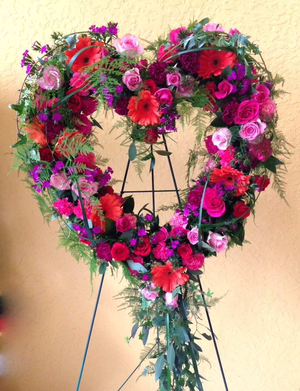 Heart-shaped floral wreath with pink and red flowers on a stand