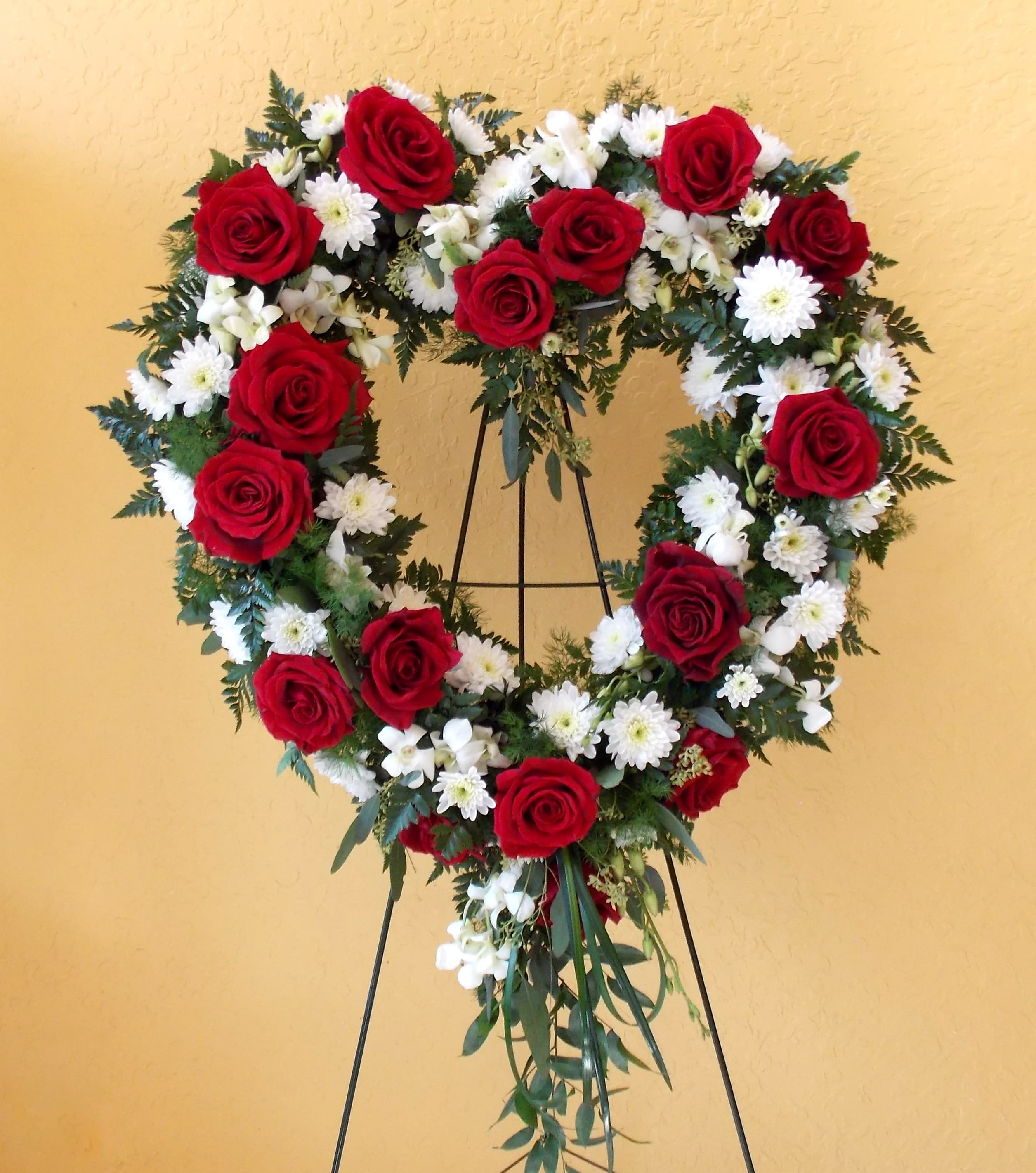 Heart-shaped wreath of red roses and white daisies on a stand