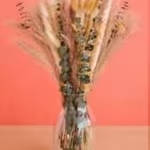 Naturally Dried Mixed Floral Vase - A breezy bundle vase of naturally dried botanicals gives a minimalist, rustic touch to any room - perfect as an everyday decorative arrangement or a thoughtful housewarming gift. This dried floral arrangement works beautifully for those who prefer low-maintenance, earthy décor and makes a calming accent for living rooms, entryways, or home offices.  The stems are a loose vertical spray of dried grasses, seed heads, etc. in muted beige, tan, dusty green and soft pink accents, tied together for a casual, sculptural silhouette. Ideal for someone who loves natural, long-lasting décor - order the size shown for a subtle focal point or add a taller vase for more presence.