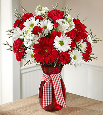 Red and white daisy bouquet in a red vase with a gingham ribbon