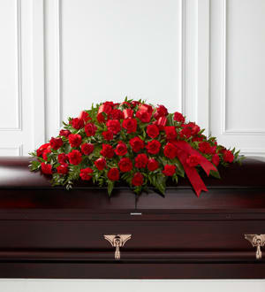 Red rose casket spray with a red ribbon on a dark casket