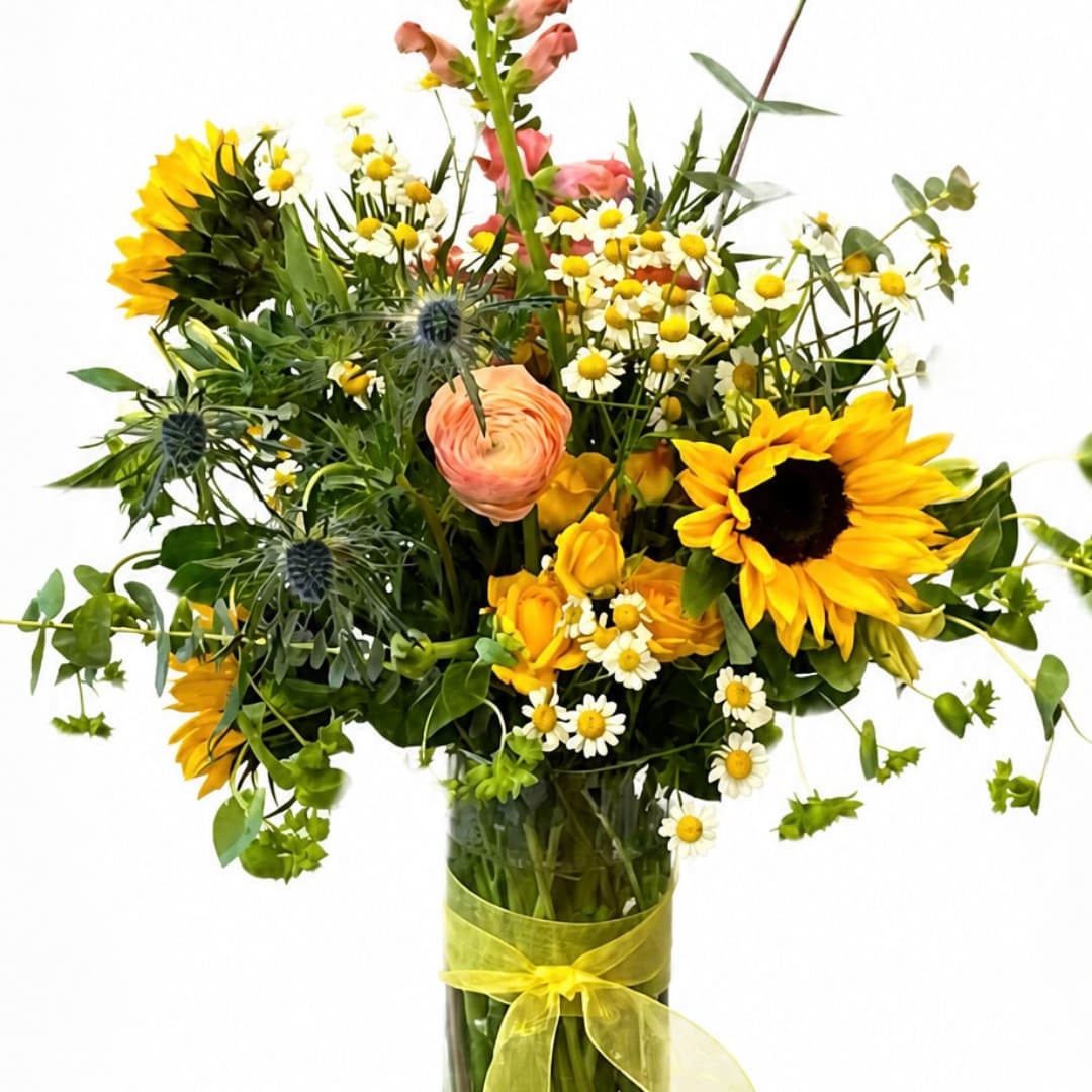Mixed bouquet with sunflowers, daisies, and peach blooms in a glass vase