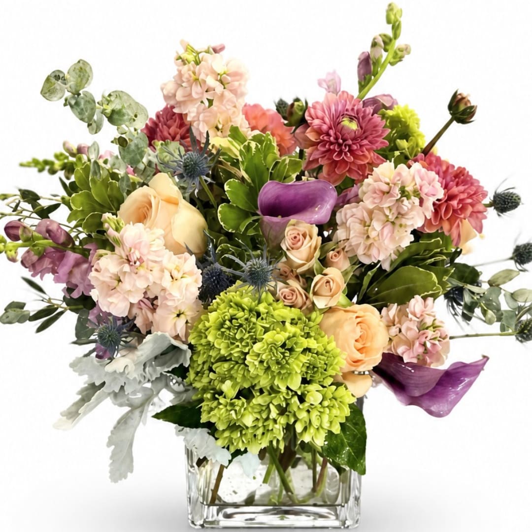 Mixed bouquet in a clear square vase with pink, peach, purple, and green blooms