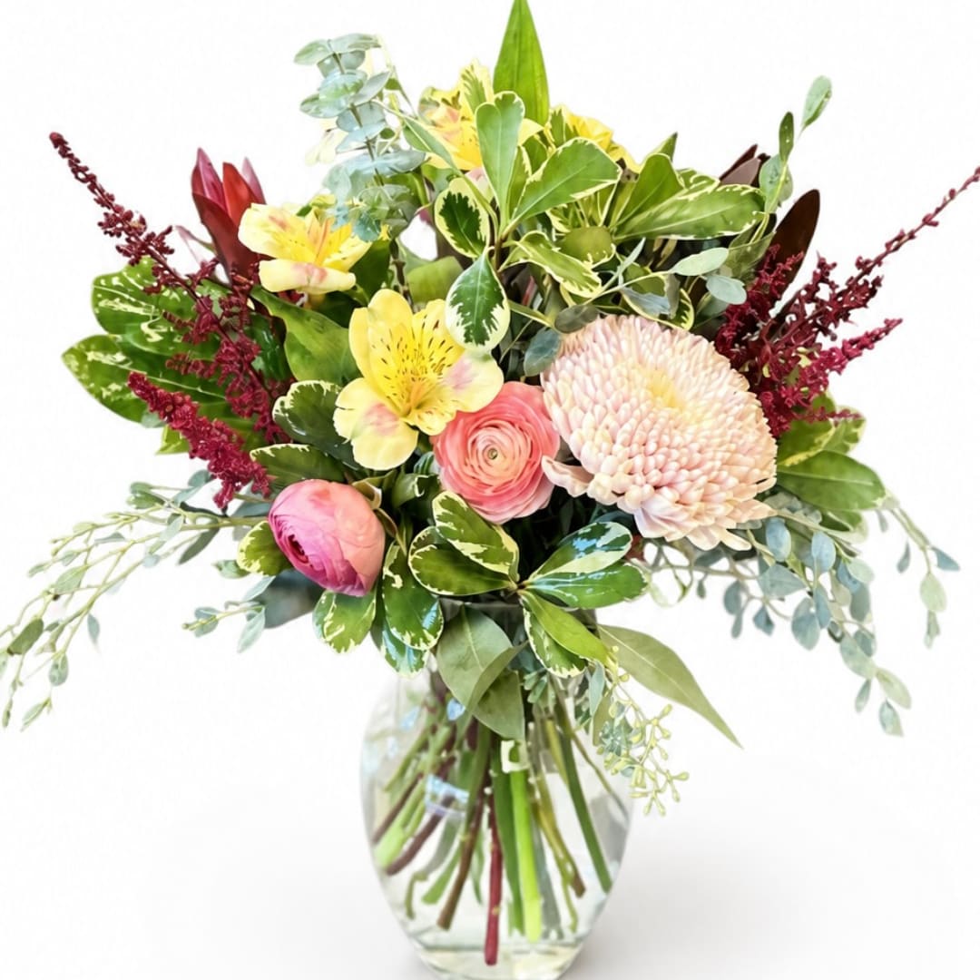 Mixed bouquet of pink and yellow flowers in a clear glass vase