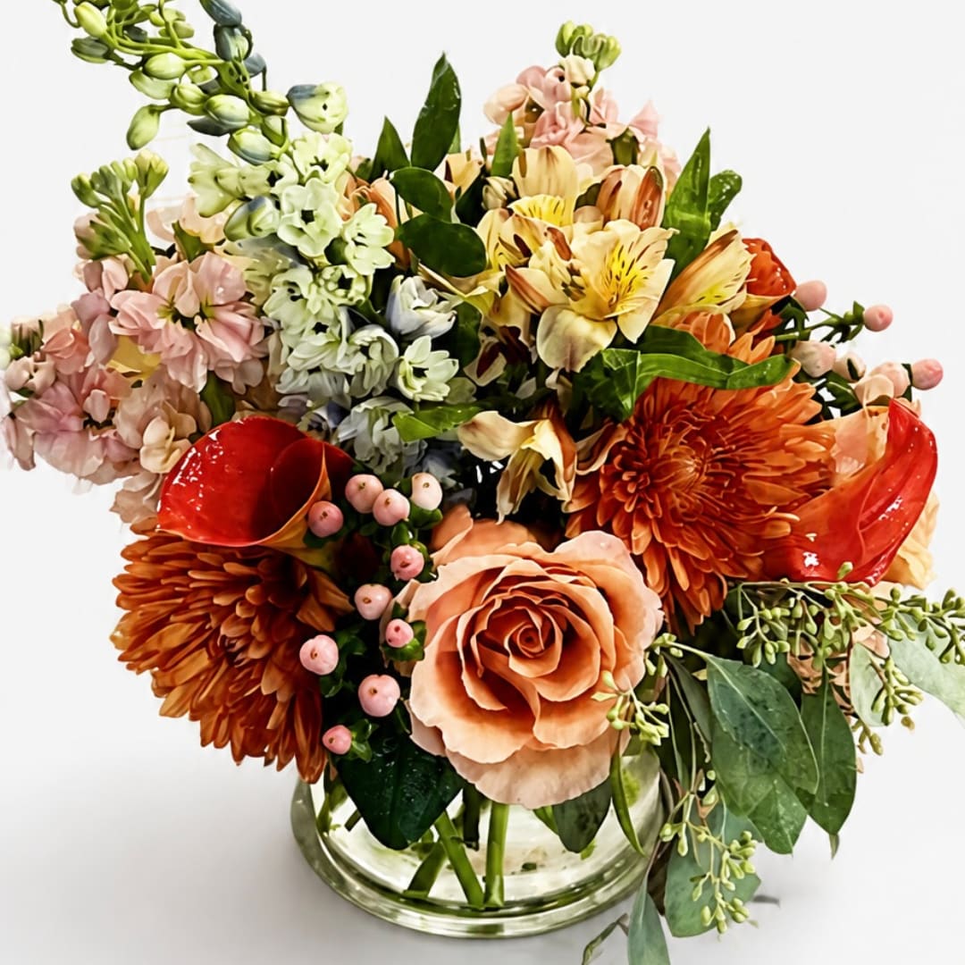 Mixed bouquet in a clear glass vase with peach, orange, pink, and cream blooms