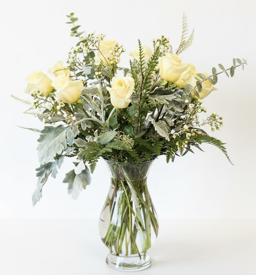 Yellow roses arranged in a clear glass vase with mixed greenery