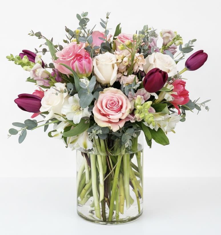 Mixed bouquet of pink, white, and burgundy flowers in a clear glass vase