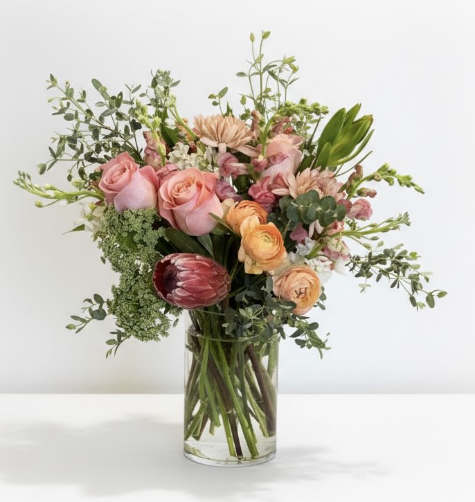 Mixed bouquet of pink and peach flowers in a clear glass vase
