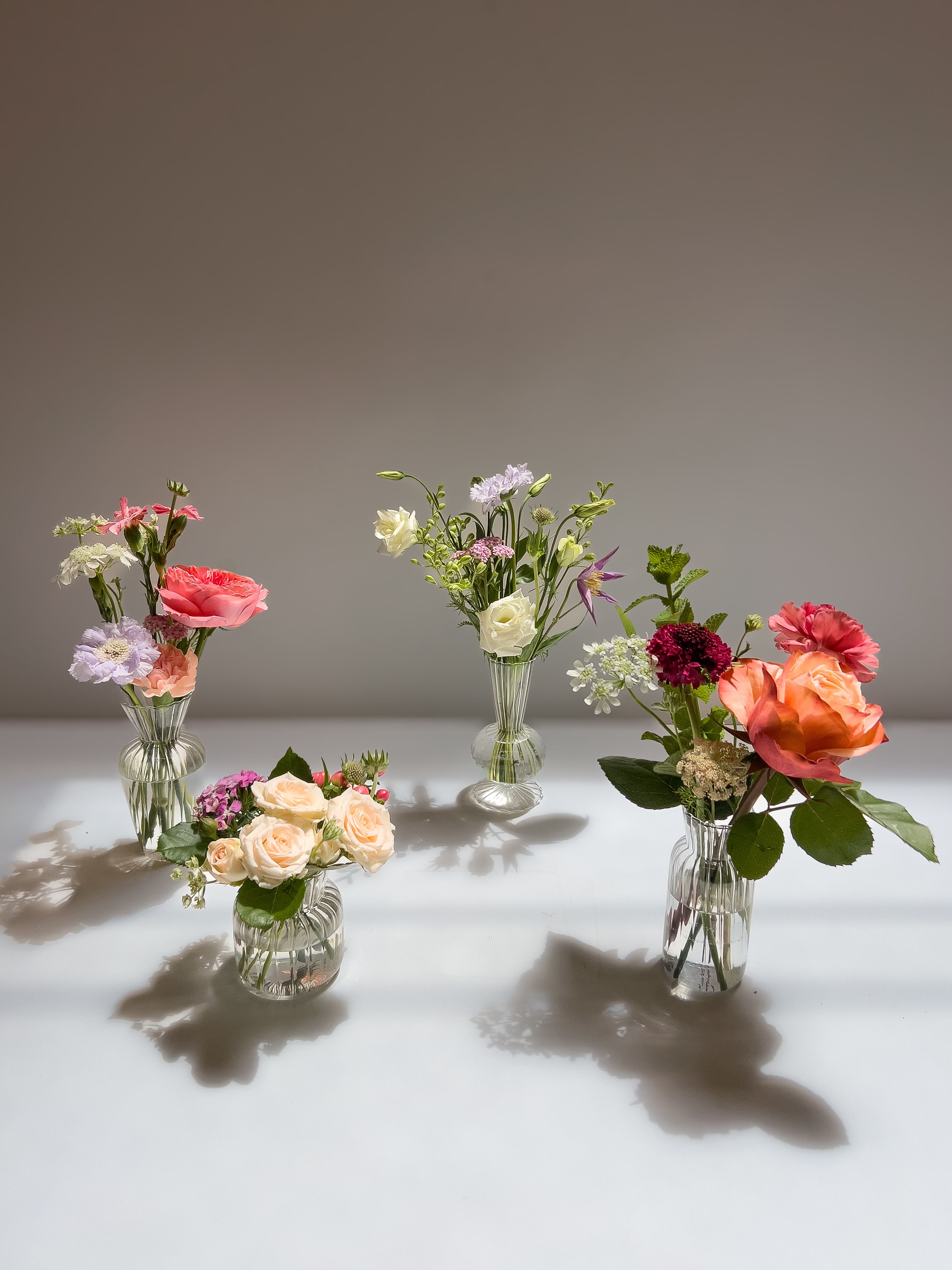 Set of small mixed flower arrangements in clear ribbed glass vases on a light surface