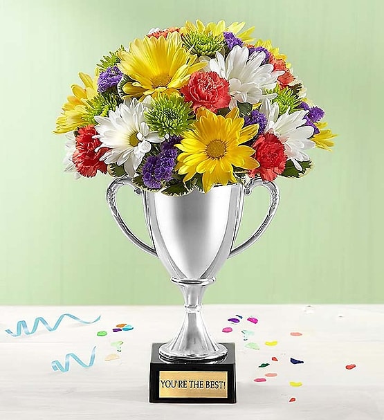 TROPHY BOUQUET™ YOU’RE THE BEST - EXCLUSIVE Here’s a winning gift to congratulate family, friends and co-workers of all ages! A vibrant mix of orange mini carnations, white and yellow daisy poms, purple statice and more are artistically hand-designed in a unique shiny silver trophy vase with a gold plaque that says, “You’re The Best!” Add a bright “Congratulations” balloon to really celebrate their special achievement.