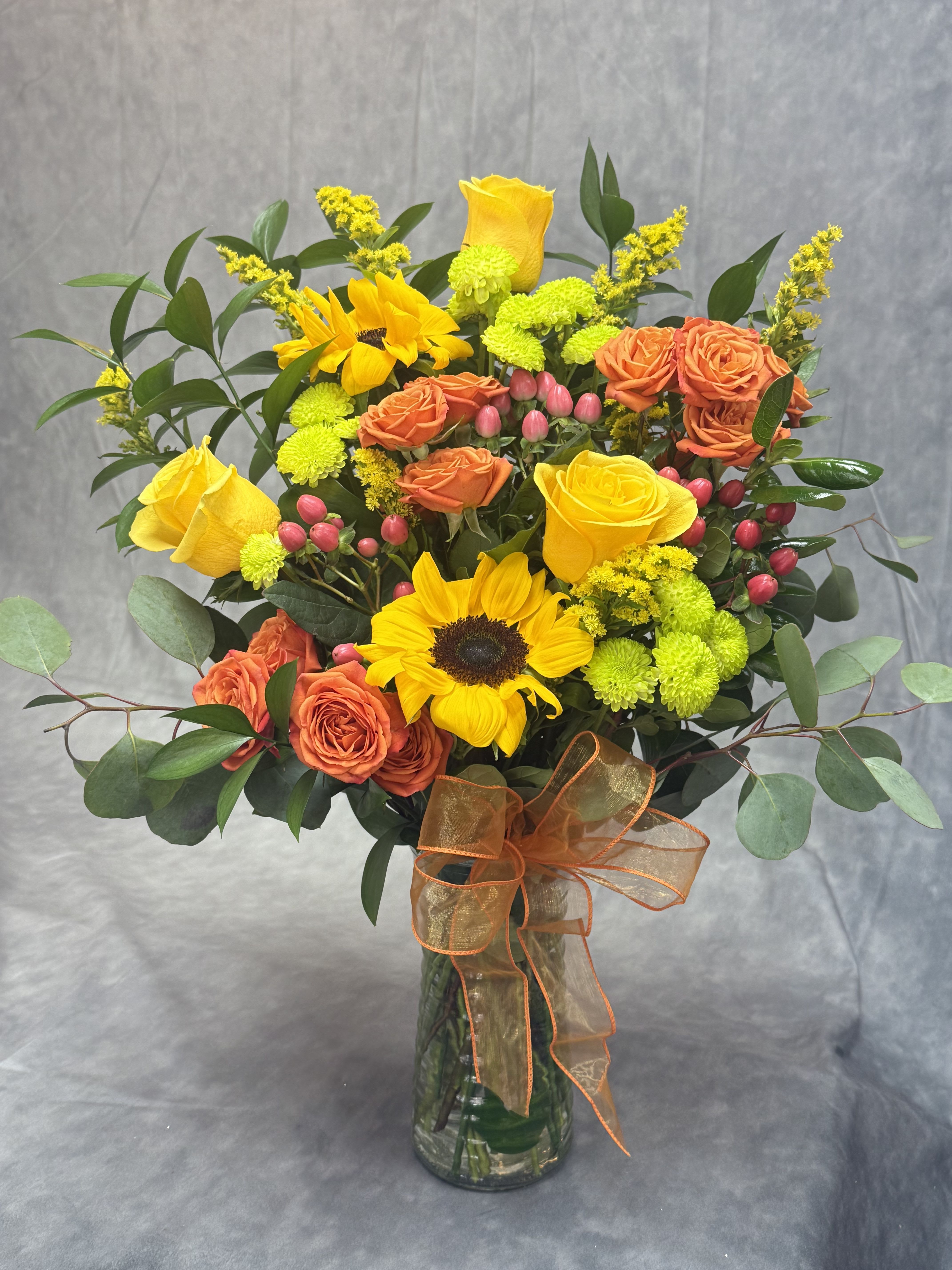 Bouquet of yellow sunflowers and orange roses in a glass vase
