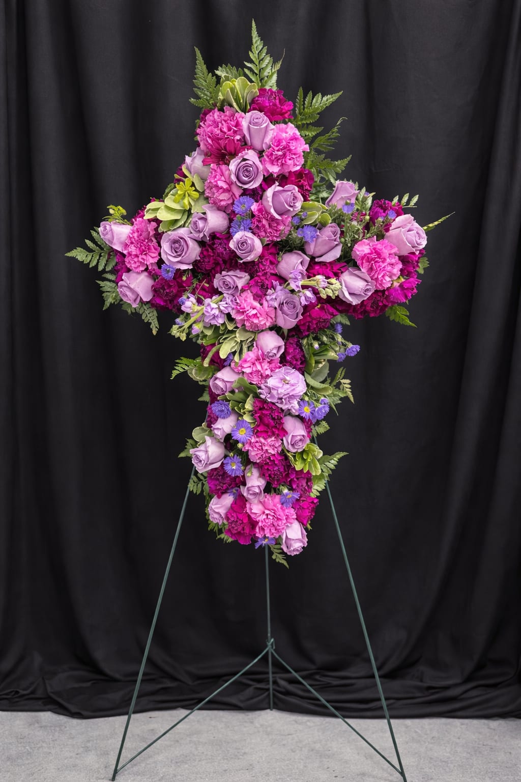 Standing cross-shaped spray of purple roses and bright pink carnations on an easel.