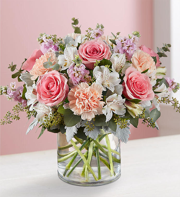 Pink roses and peach flowers arranged in a clear glass vase