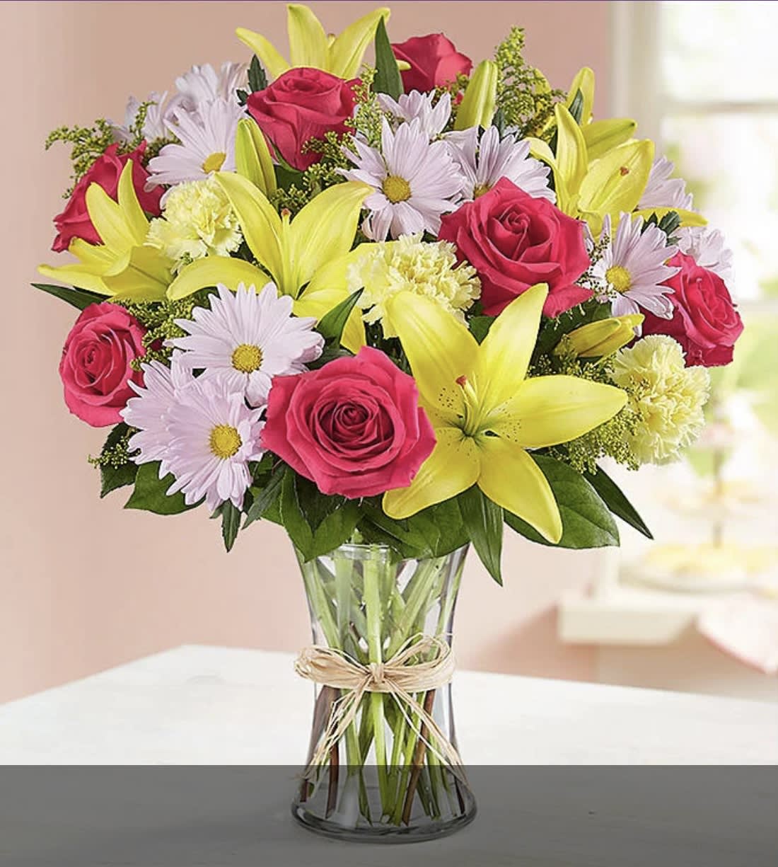 Bouquet of pink roses, yellow lilies, and pale daisies in a glass vase