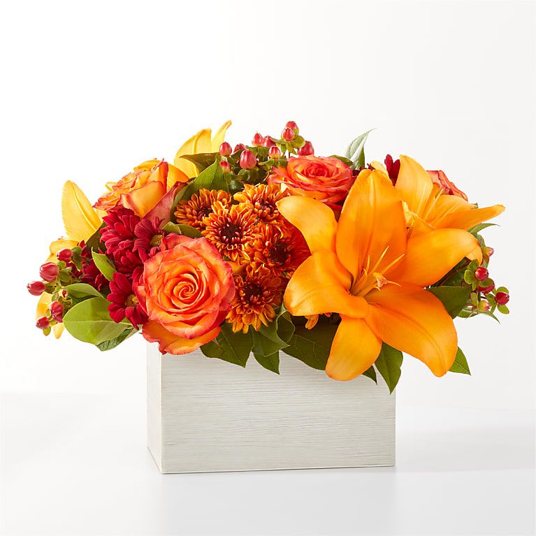 Orange and red floral arrangement in a white box