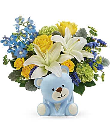 Teleflora's Sunny Cheer Bear Bouquet - Spread cheer far and near with this sunny bouquet of yellow roses and white lilies, charmingly arranged in this sweet ceramic teddy bear keepsake. Yellow roses, yellow spray roses, white asiatic lilies, green carnations, light blue delphinium, and blue sinuata statice are arranged with bupleurum, dusty miller, and lemon leaf. Delivered in a blue Bundle of Love Bear.