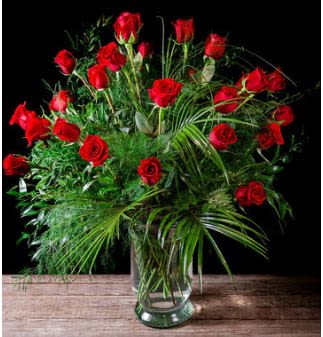Red roses arranged in a clear glass vase with lush greenery