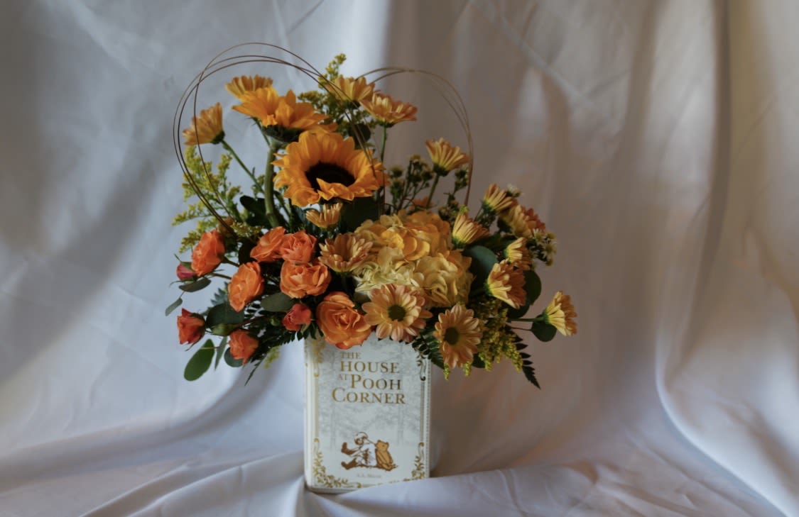 Book Lover's Blooms - Sunflowers and bright orange roses steal the show in this cheerful flower arrangement for a book lover or anyone who treasures cozy, sentimental moments. Perfect as a birthday bouquet, congratulations gift, or just-because surprise, the warm orange, sunny yellow, crisp white, and fresh green palette reads like a happy page from a favorite story-playful, nostalgic, and instantly uplifting. Flowers will vary. Choose between Wuthering Heights, Alice in Wonderland and Winnie the Pooh.