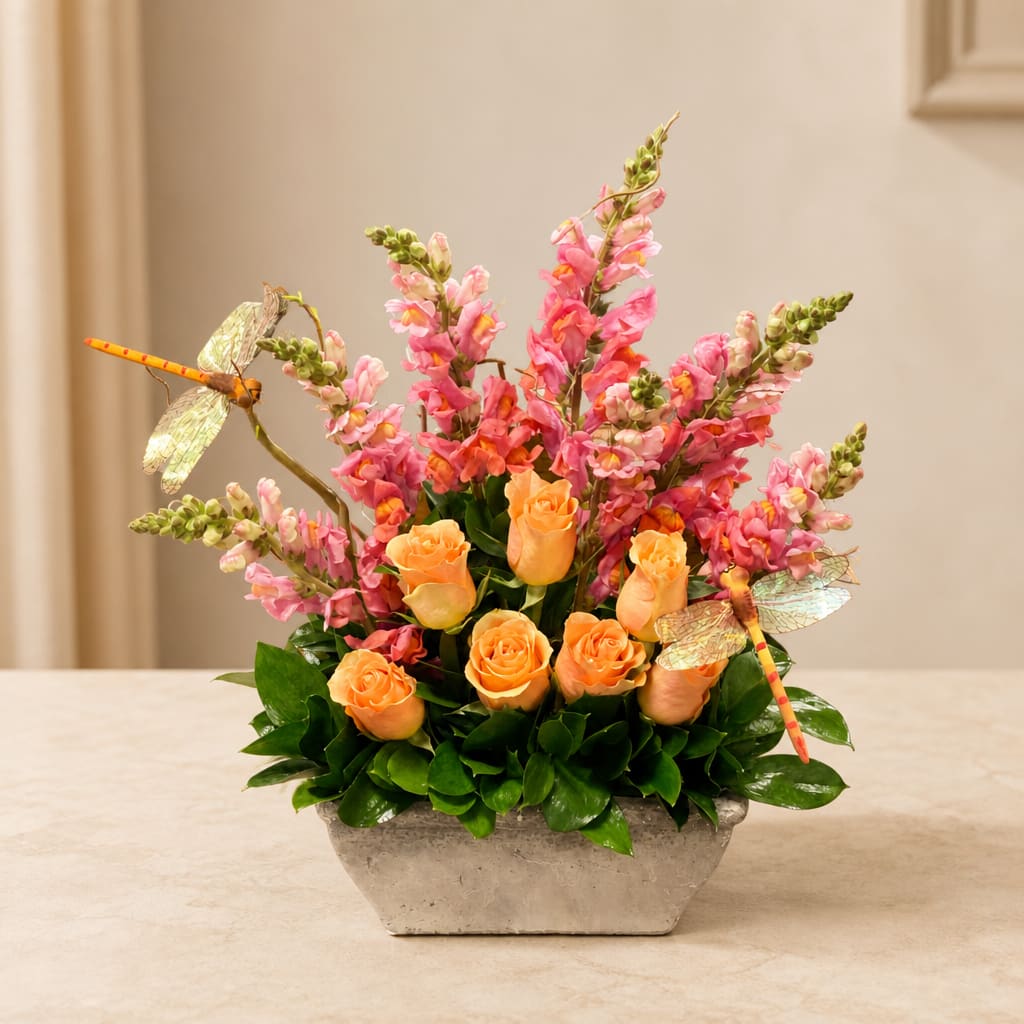 Orange roses and pink snapdragons in a rectangular vase with dragonfly picks