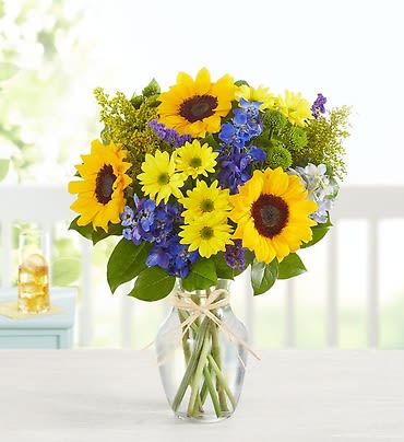 Sunflowers and blue flowers in a clear glass vase with a ribbon
