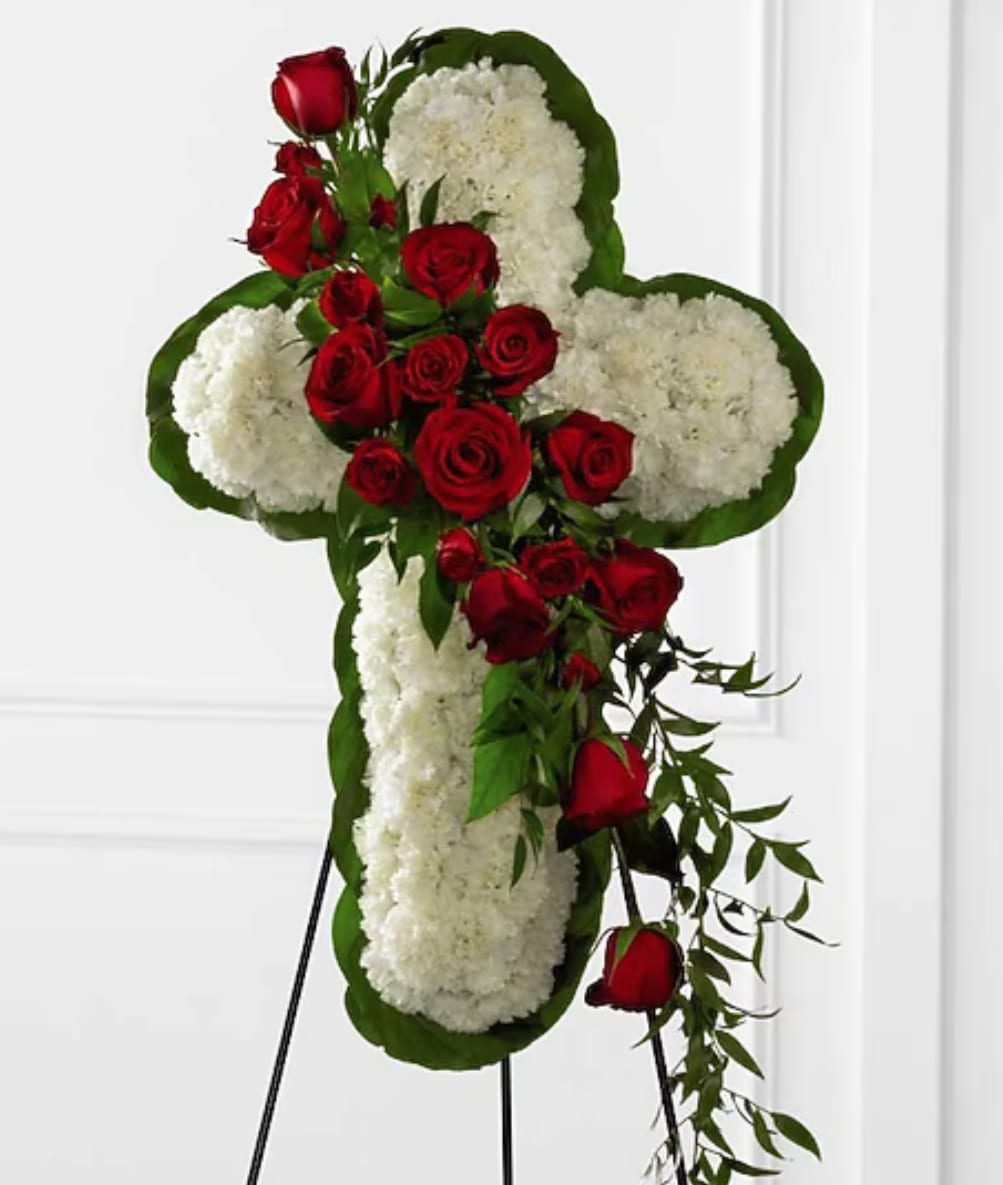  CROSS STANDING SPRAY - A striking cross-shaped standing spray arranged on a floral easel, this sympathy flower arrangement pairs deep red roses with dense white blooms to create a solemn, respectful tribute for a funeral or memorial service. The red-and-white color contrast reads as classic and dignified, making it a clear expression of sympathy and remembrance for the person you're honoring.  Clusters of red roses sit amid plentiful white flowers, all shaped into a bold cruciform silhouette with broad green edging and trailing greenery for soft movement. Mounted on a sturdy floral stand, the spray presents at a prominent height suitable for viewing near a casket or at a service; sizes and final proportions may vary slightly by availability but are assembled to preserve the cross shape and visual balance.  Choose this standing cross to convey heartfelt condolences and to celebrate a life with traditional, meaningful symbolism; it's the kind of tribute that helps mourners feel acknowledged and remembered. For delivery and placement at services, please confirm date, venue instructions, and any preferred message so we can ensure timely, respectful presentation.