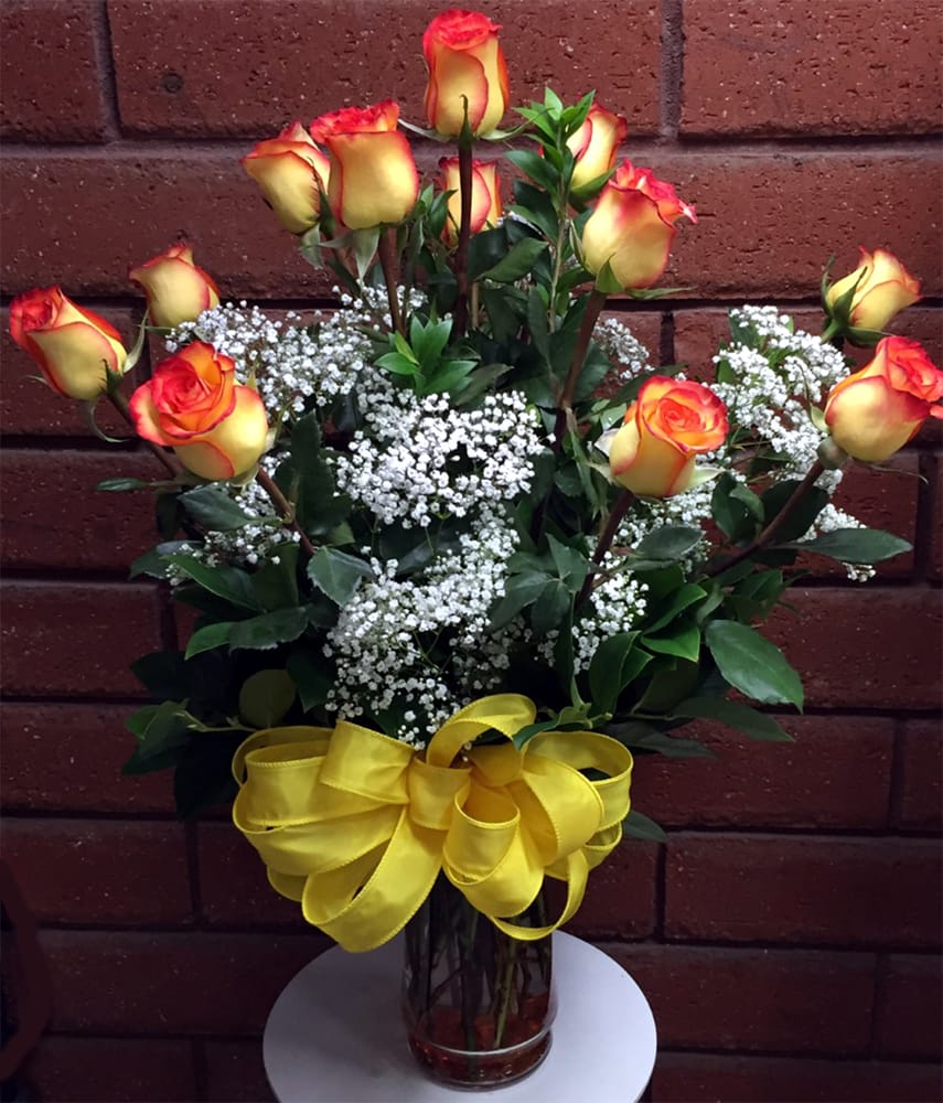 Yellow and red roses in a glass vase with baby's breath and a yellow ribbon