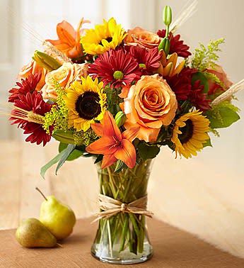 Mixed bouquet of sunflowers, roses, lilies, and red daisies in a glass vase