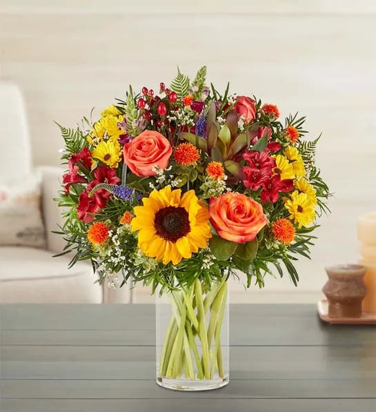 Charming Fall Foliage Bouquet - Our charming autumn bouquet showcases the season’s striking textures and colors. A unique blend of blooms is loosely gathered in a clear vase, warming hearts and homes with its rich beauty.  All-around arrangement with sunflowers, red Leucadendron and Peruvian lilies (alstroemeria), orange and bi-color yellow roses, yellow Viking poms, purple snapdragons and Veronica, white Limonium, orange safflower; accented with red hypericum, curly willow tips and assorted greenery. Artistically designed in a clear glass cylinder vase; measures 8"H Large arrangement measures approximately 26"H x 24"W Medium arrangement measures approximately 24"H x 21"W Small arrangement measures approximately 23"H x 20"W To ensure lasting beauty, Peruvian lilies (alstroemeria) may arrive in bud form and will fully bloom over the next few days Sunflowers may have light or dark centers