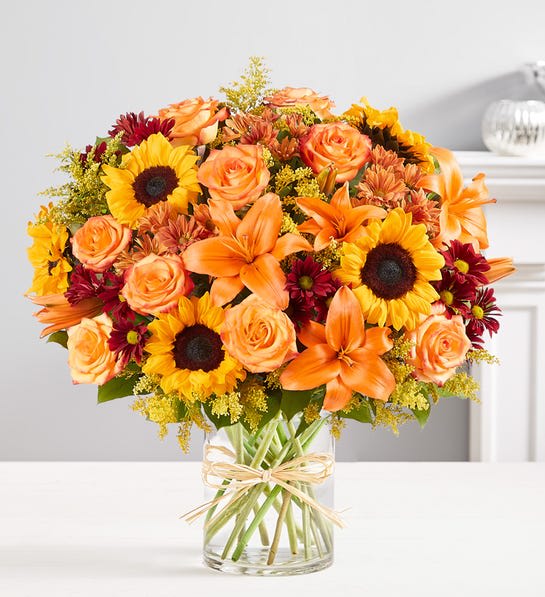 Bouquet of orange roses, lilies, and sunflowers in a clear glass vase