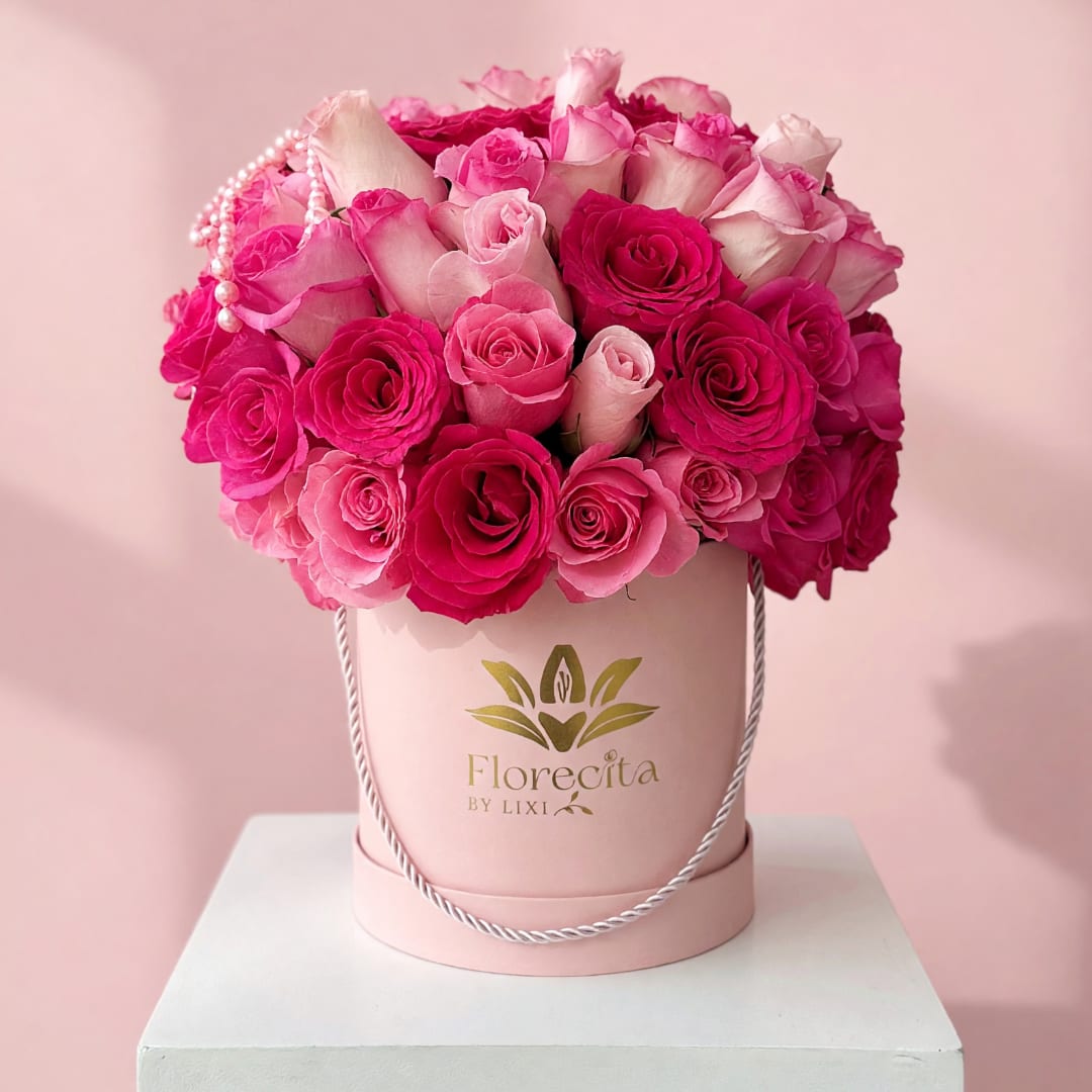 Pink and white roses arranged in a round hatbox with a pearl strand