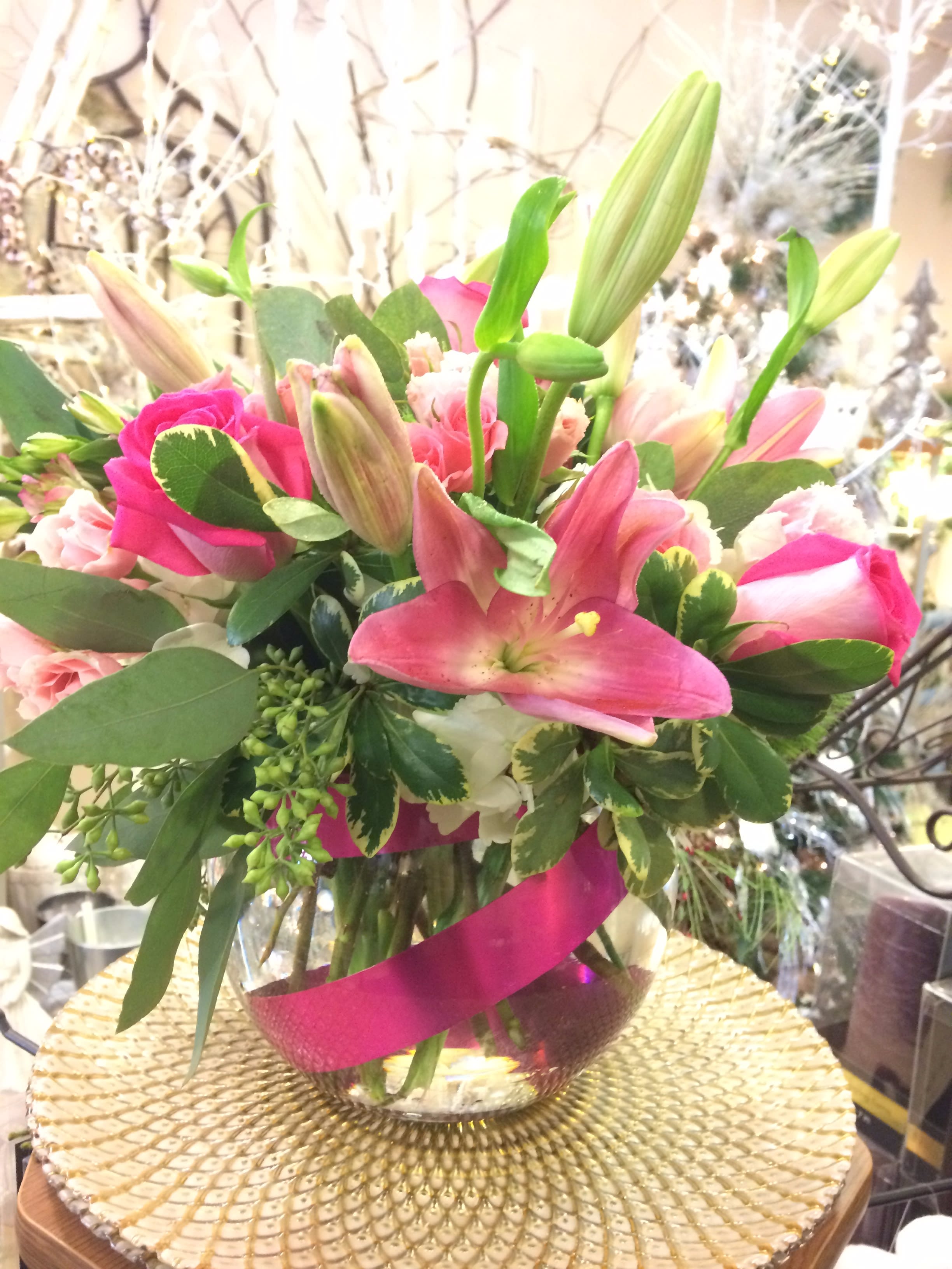 Pink lilies and roses arranged in a glass vase with a magenta ribbon