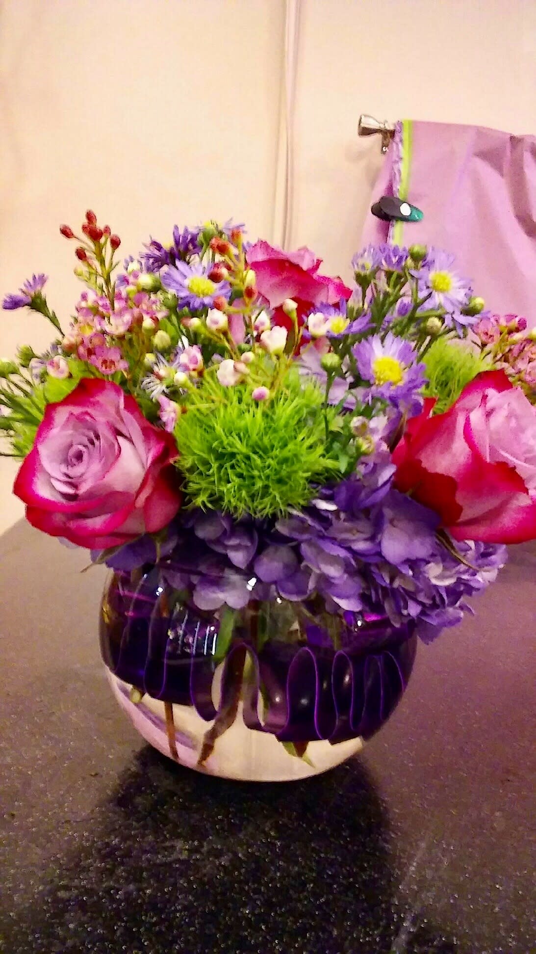 Bouquet of pink roses, purple daisies, and green filler in a round vase