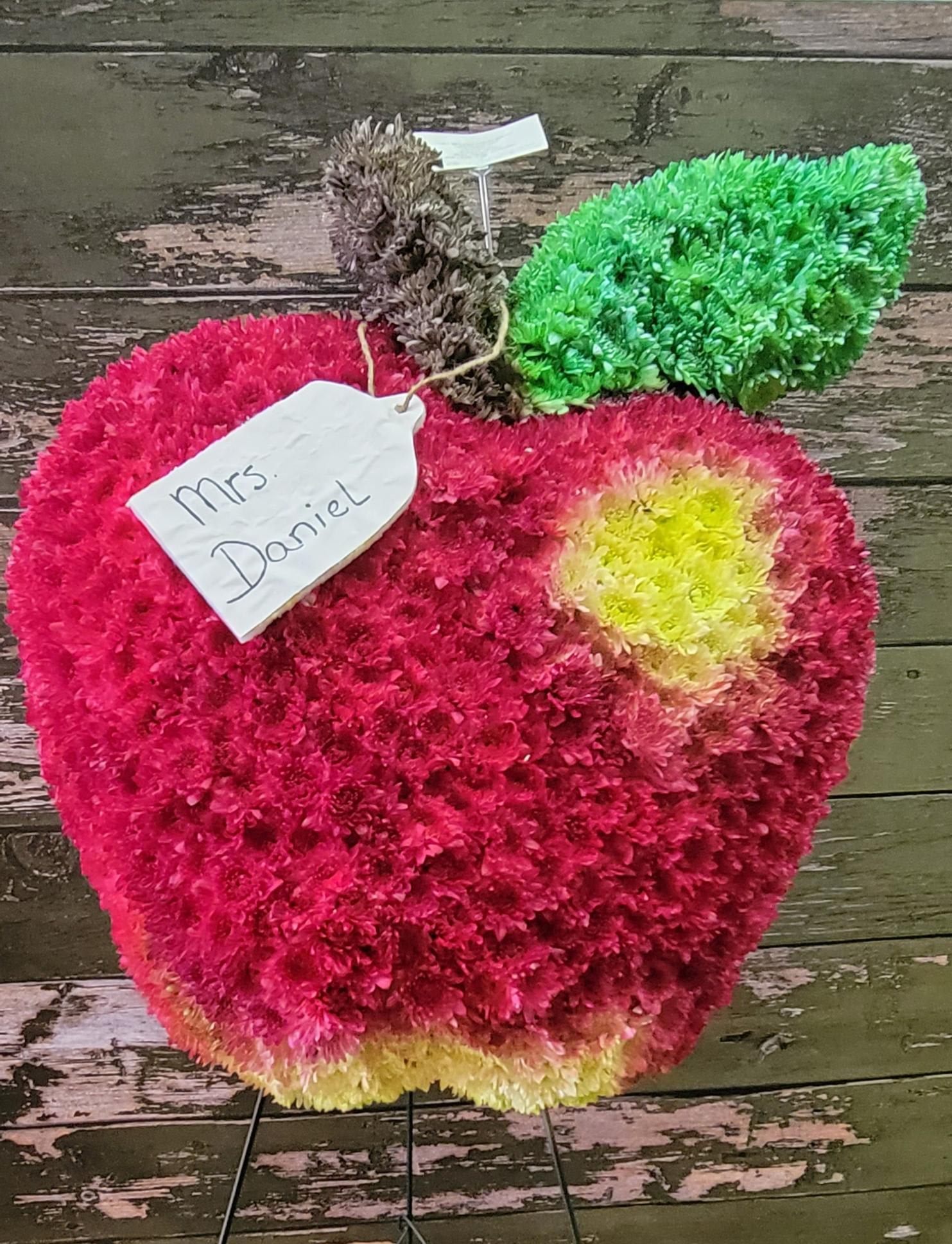 Apple-shaped floral arrangement in pink, green, and yellow with a name tag